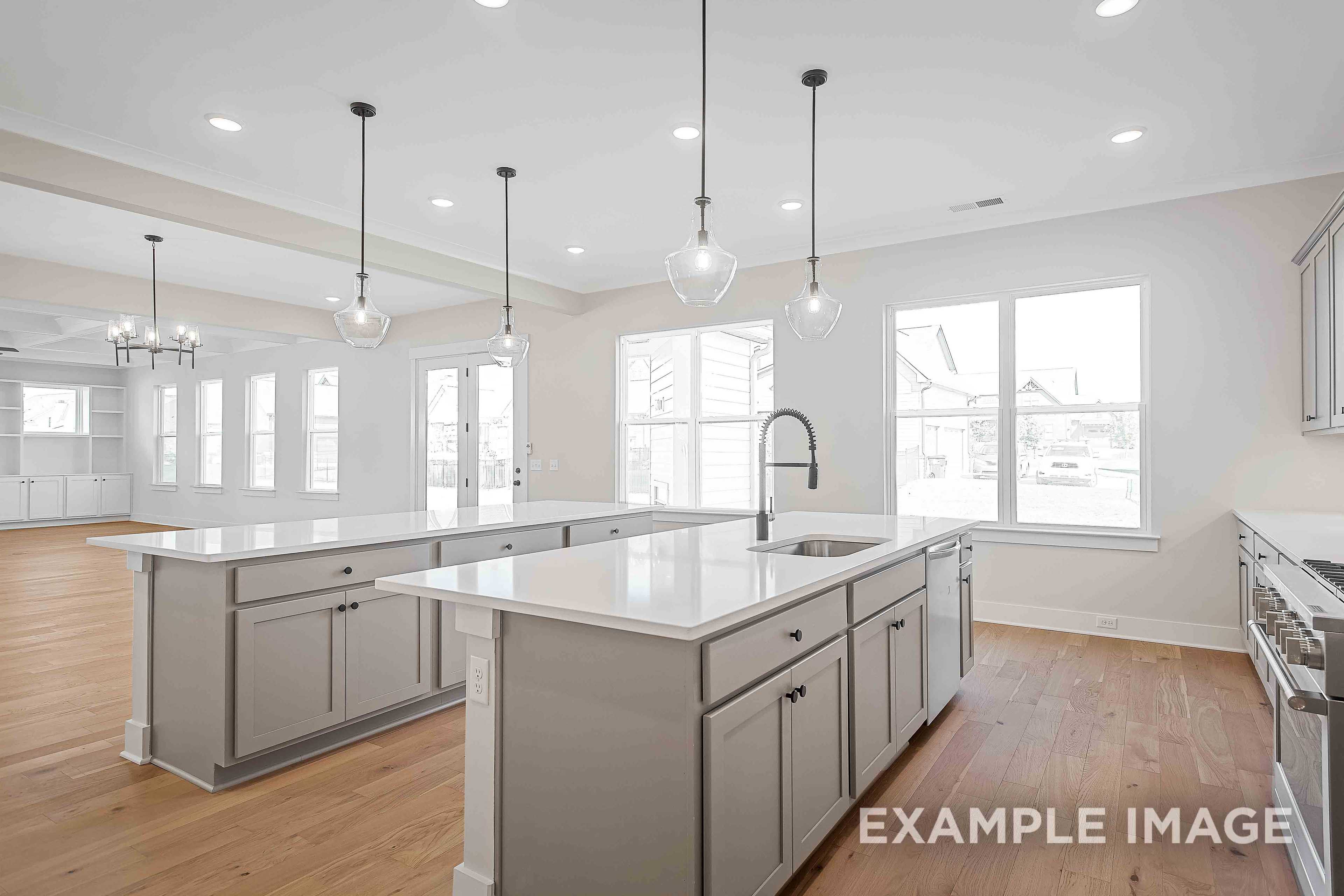 Spacious Alston A kitchen by Davidson Homes featuring large white island with sink, gray shaker cabinets, pendant lights, and open layout with hardwood floors