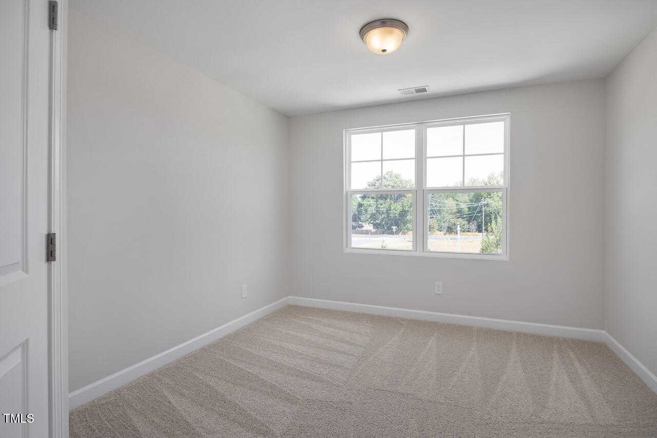 Bright secondary bedroom with gray walls, carpeted floor, and large window overlooking trees in Davidson Homes The Graham, Fuquay-Varina, NC