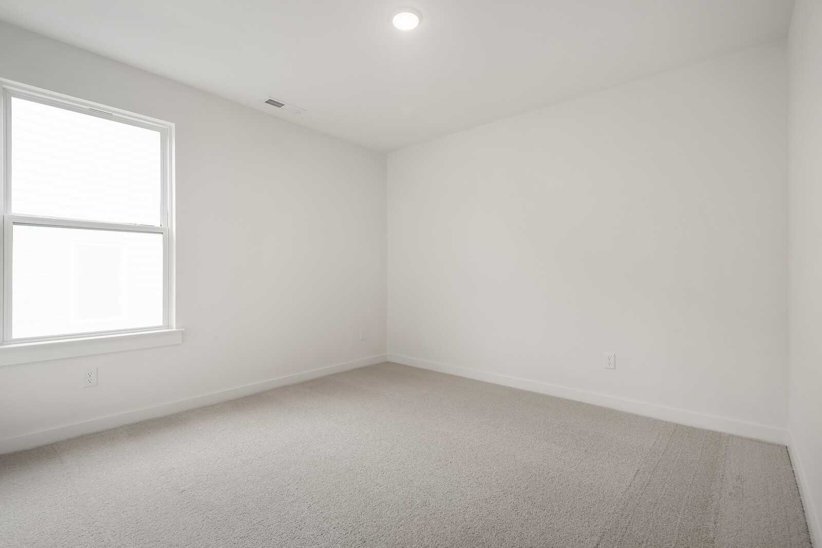 Bright empty bedroom with white walls, large double window, and neutral carpet in Davidson Homes The Logan C, Gallatin, TN
