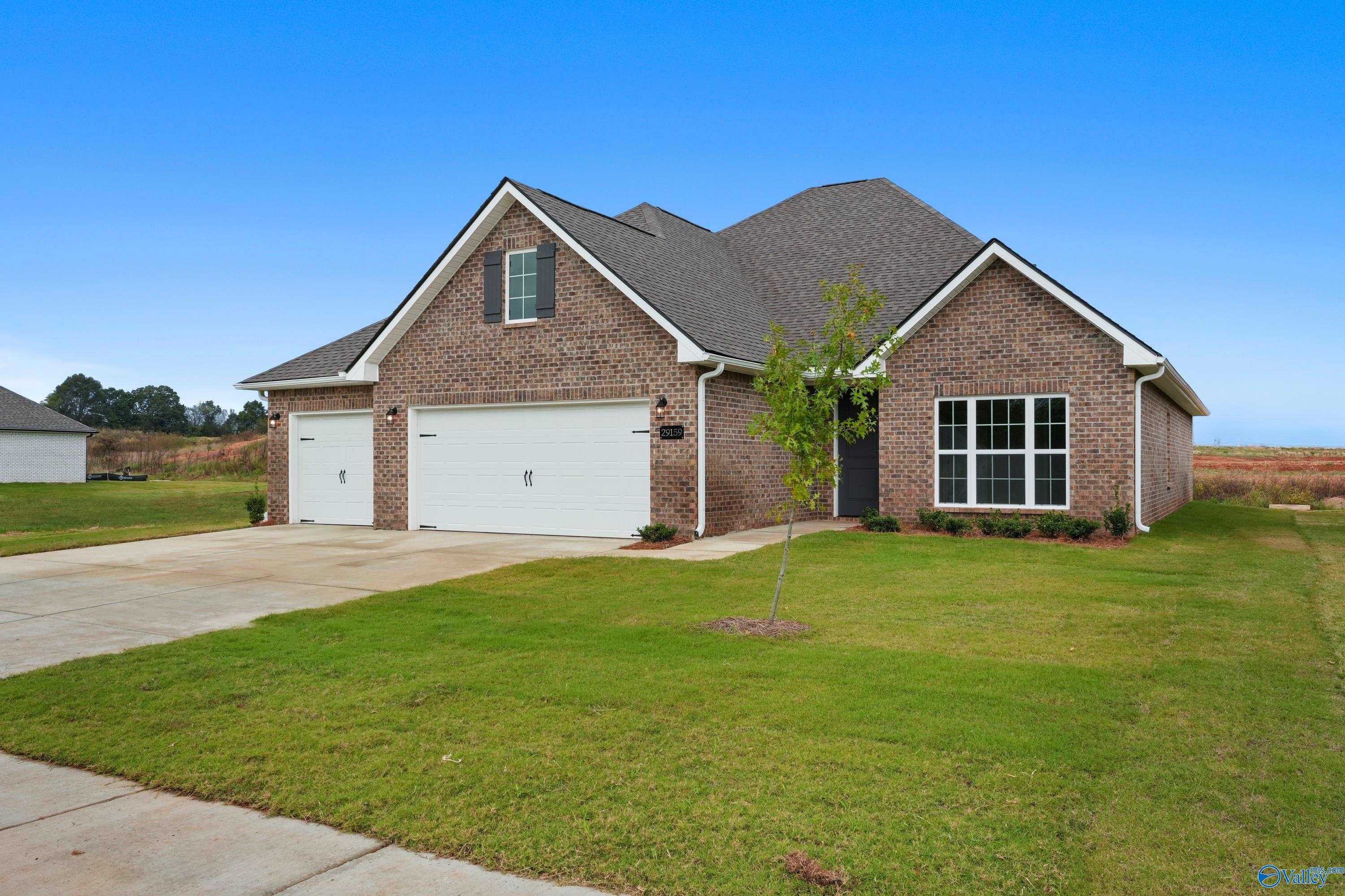 Modern brick single-story home with gabled roof, large windows, 3-car garage, driveway, and lush front yard in Creekside, Harvest, Alabama