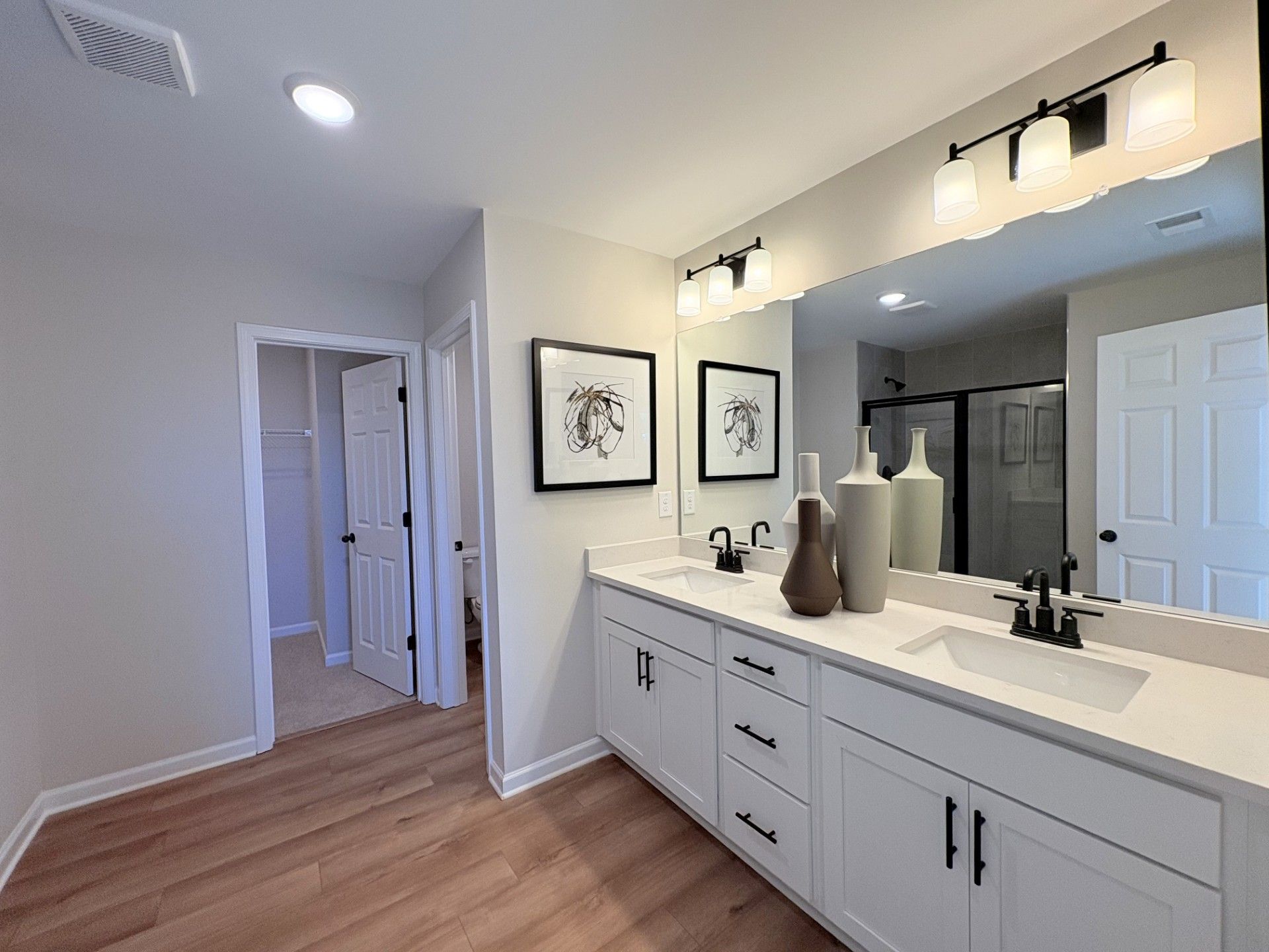 Luxury primary bathroom in Hemingway Cumming GA with double white vanity quartz counters large mirror and abstract wall art