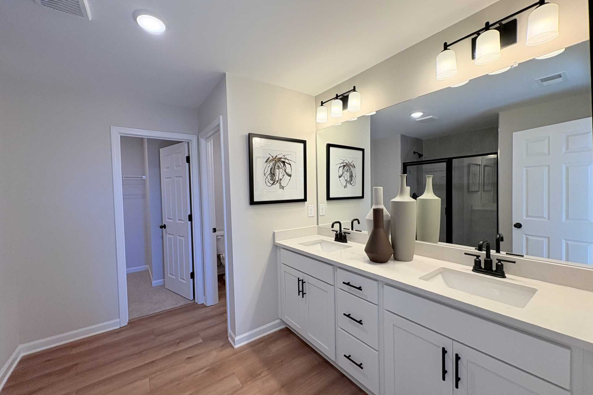 Luxury primary bathroom in Hemingway Cumming GA with double white vanity quartz counters large mirror and abstract wall art