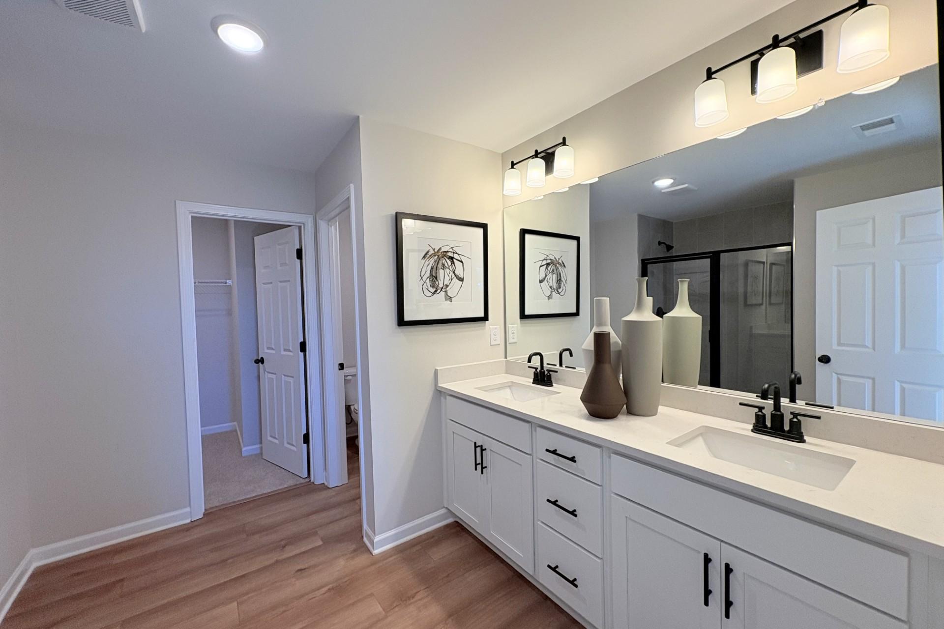 Luxury primary bathroom in Hemingway Cumming GA with double white vanity quartz counters large mirror and abstract wall art