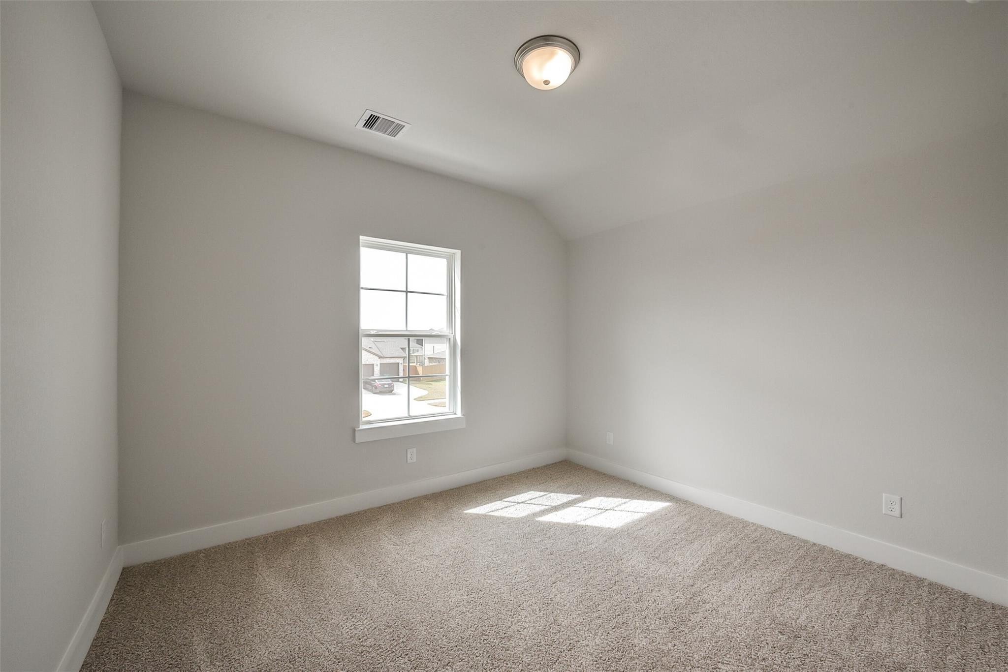 Bright empty bedroom with sloped ceiling, window sunlight, beige carpet in Davidson Homes The Philip B, Rosharon, Texas