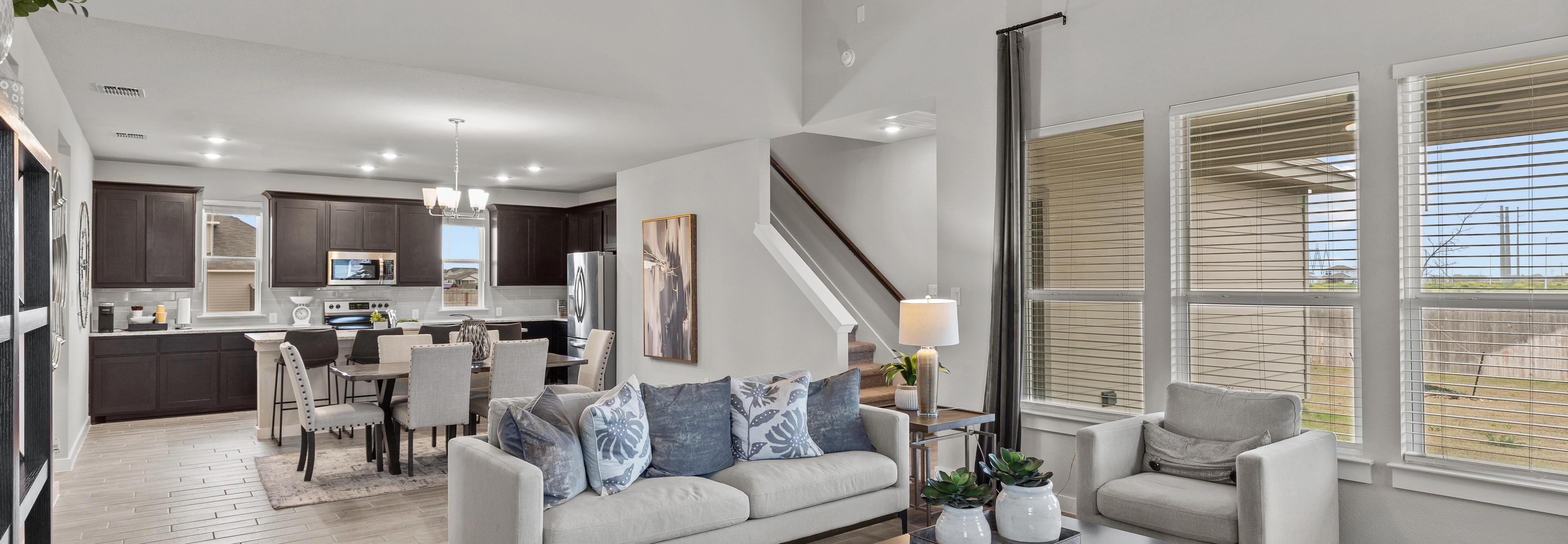 Open-concept living kitchen dining area at Hannah Heights in Seguin Texas with gray sofa dark cabinets hardwood floors large windows