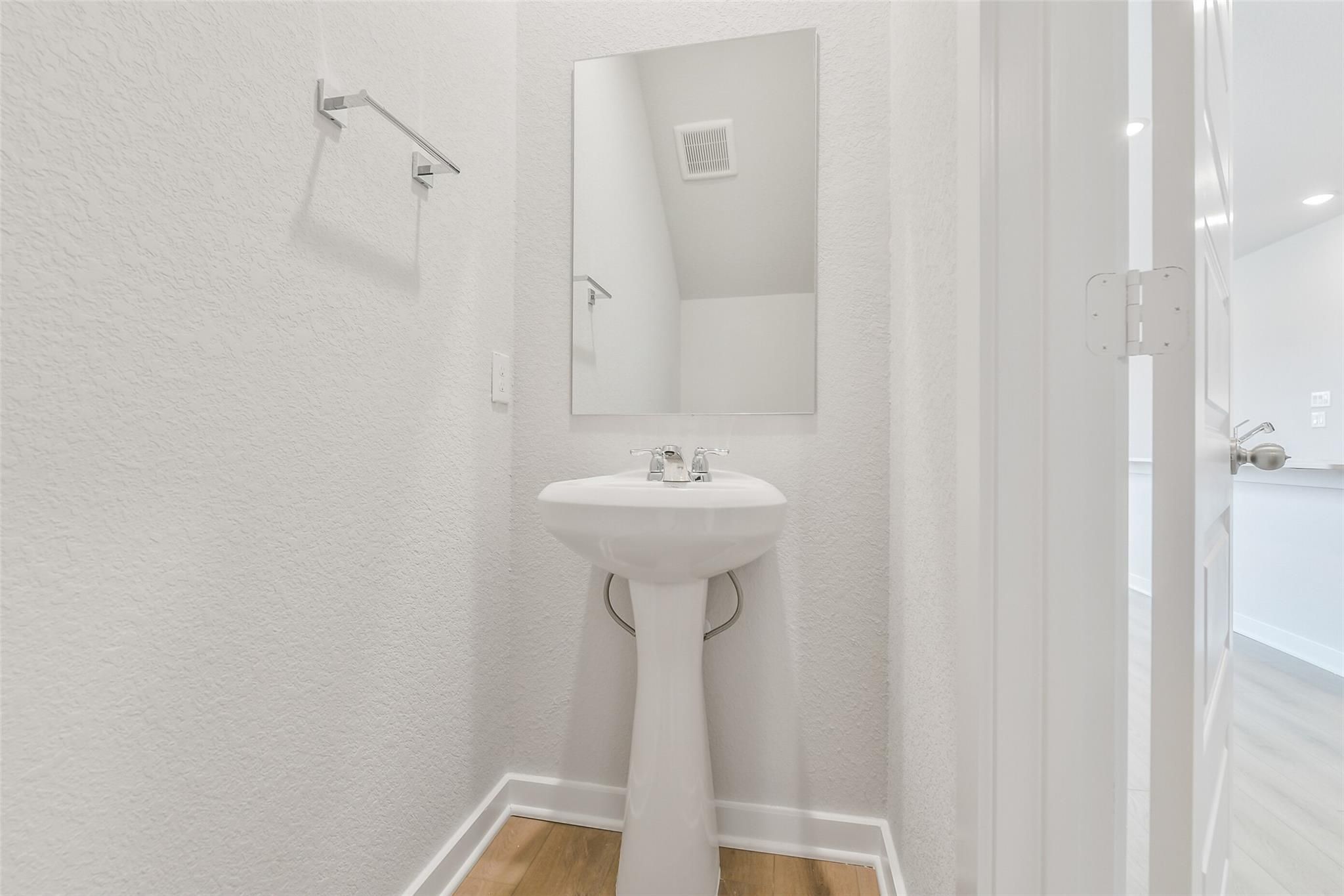 Compact powder room with white pedestal sink, mirror, and towel bar in Davidson Homes The Brazos E, Liberty Estates, Cleveland, Texas