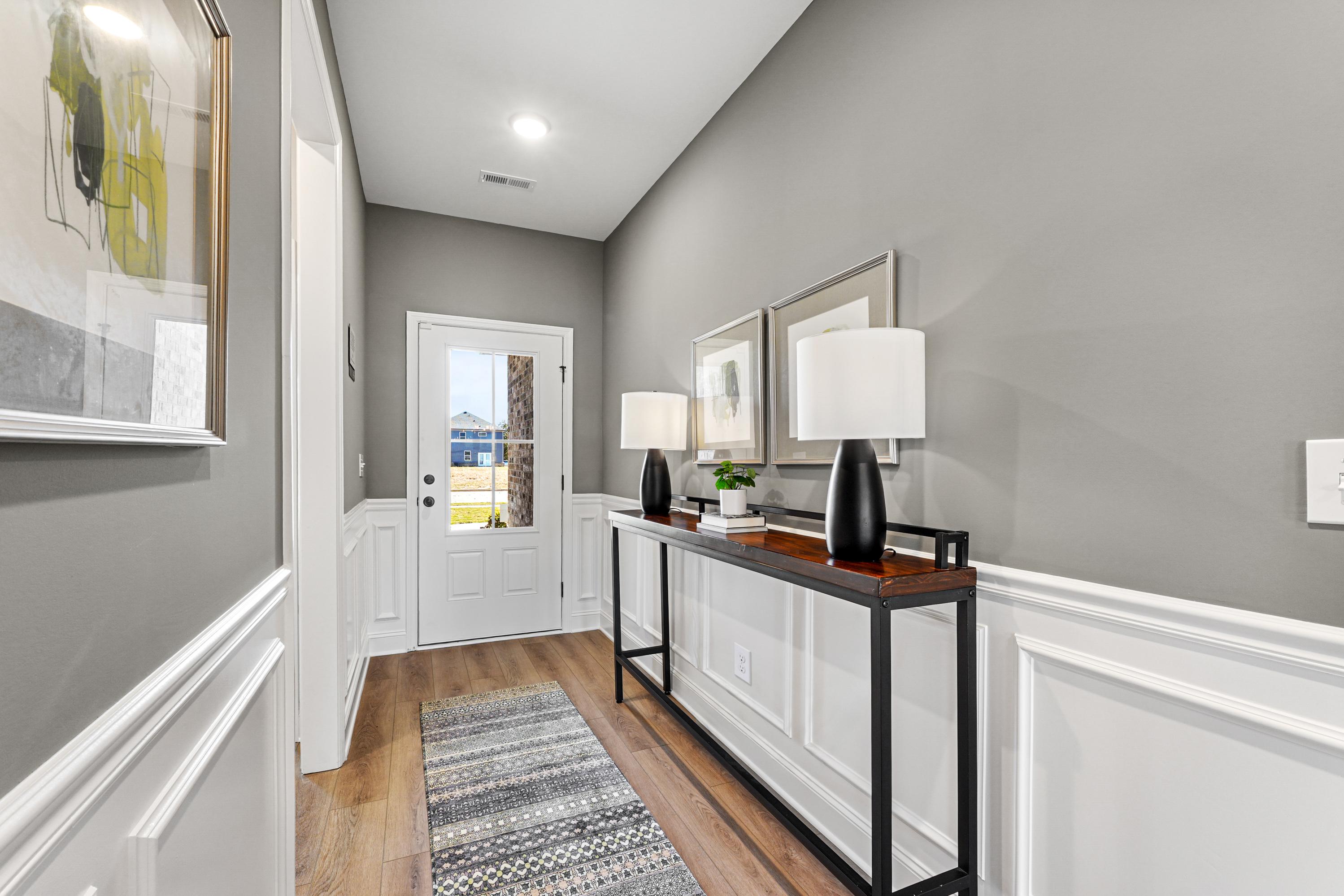 Modern entry foyer at Ramsay Cove in Owens Cross Roads, Alabama with gray walls, hardwood floors, white front door, and console table with lamps