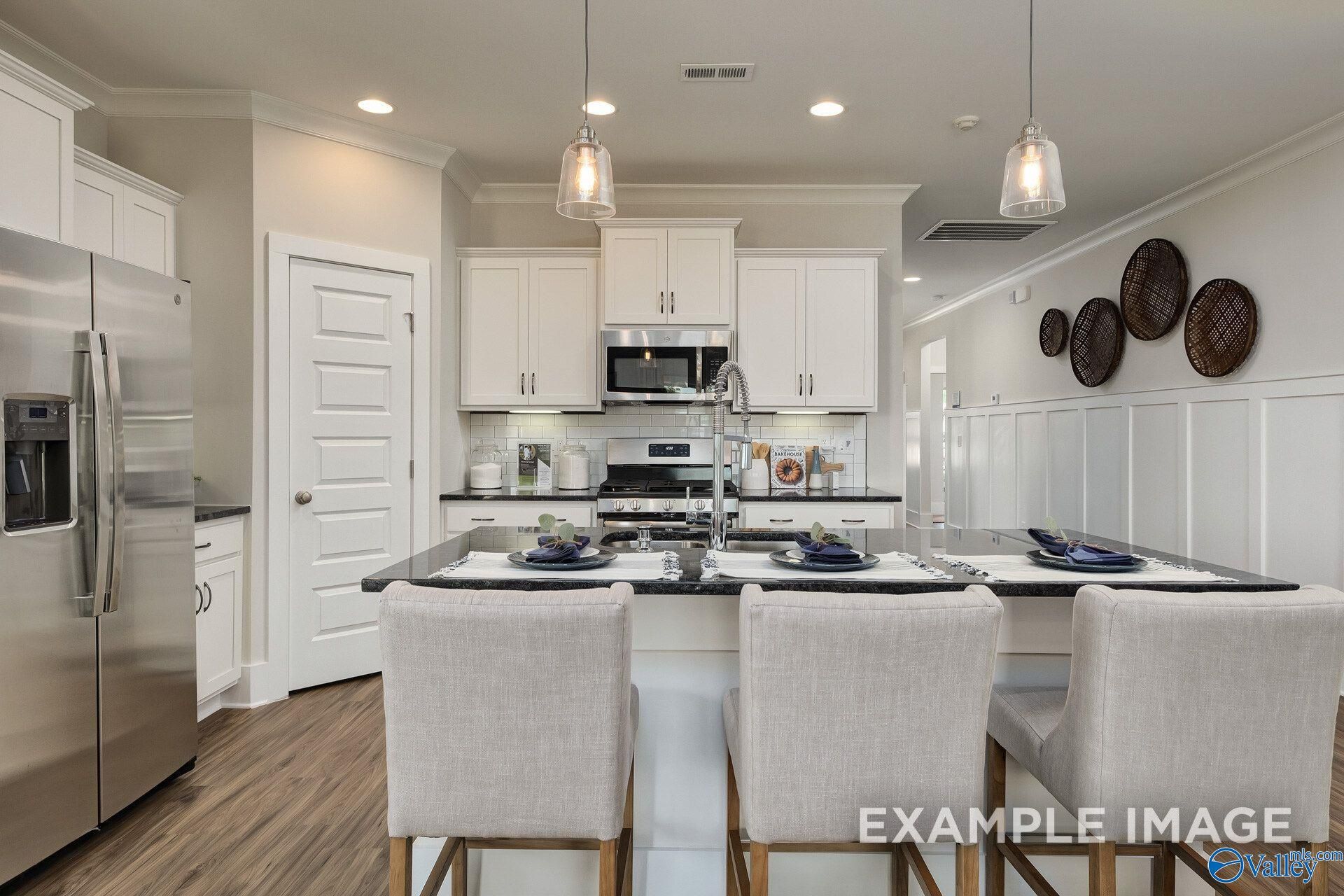 White kitchen with granite island, pendant lights, and stainless appliances in Davidson Homes The Daphne D, Toney, Alabama