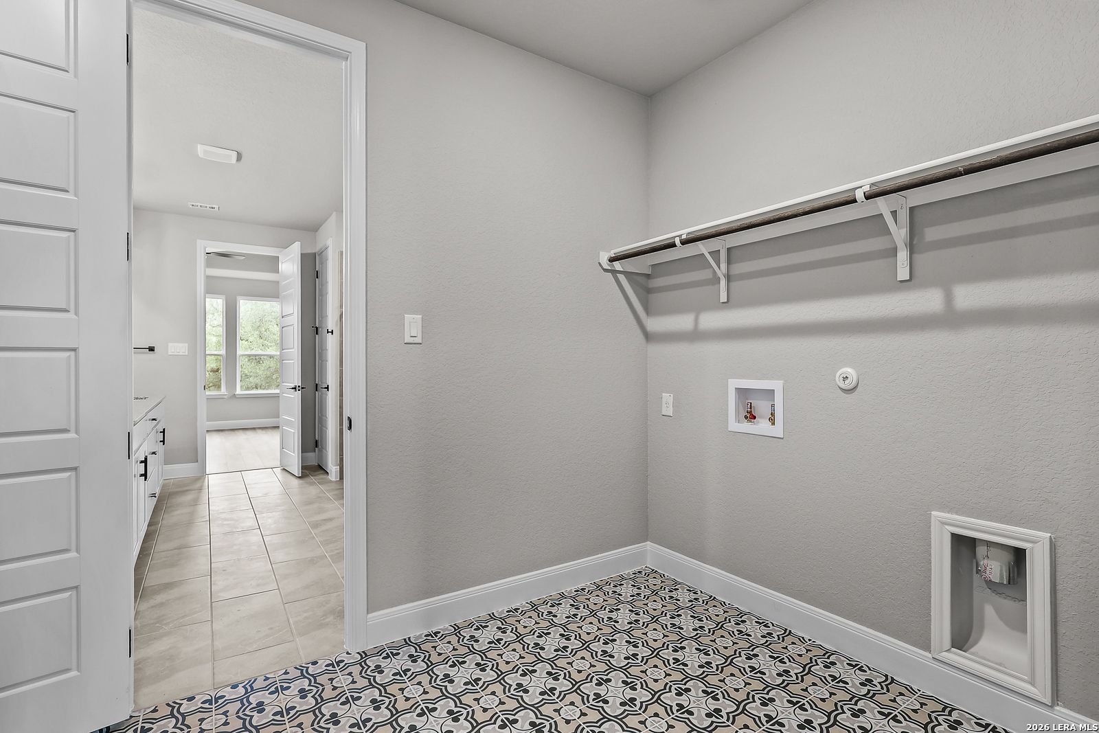 Modern laundry room featuring utility sink, washer/dryer hookups, hanging rod, and blue patterned tile floor in Davidson Homes The Belmont H, Castroville TX