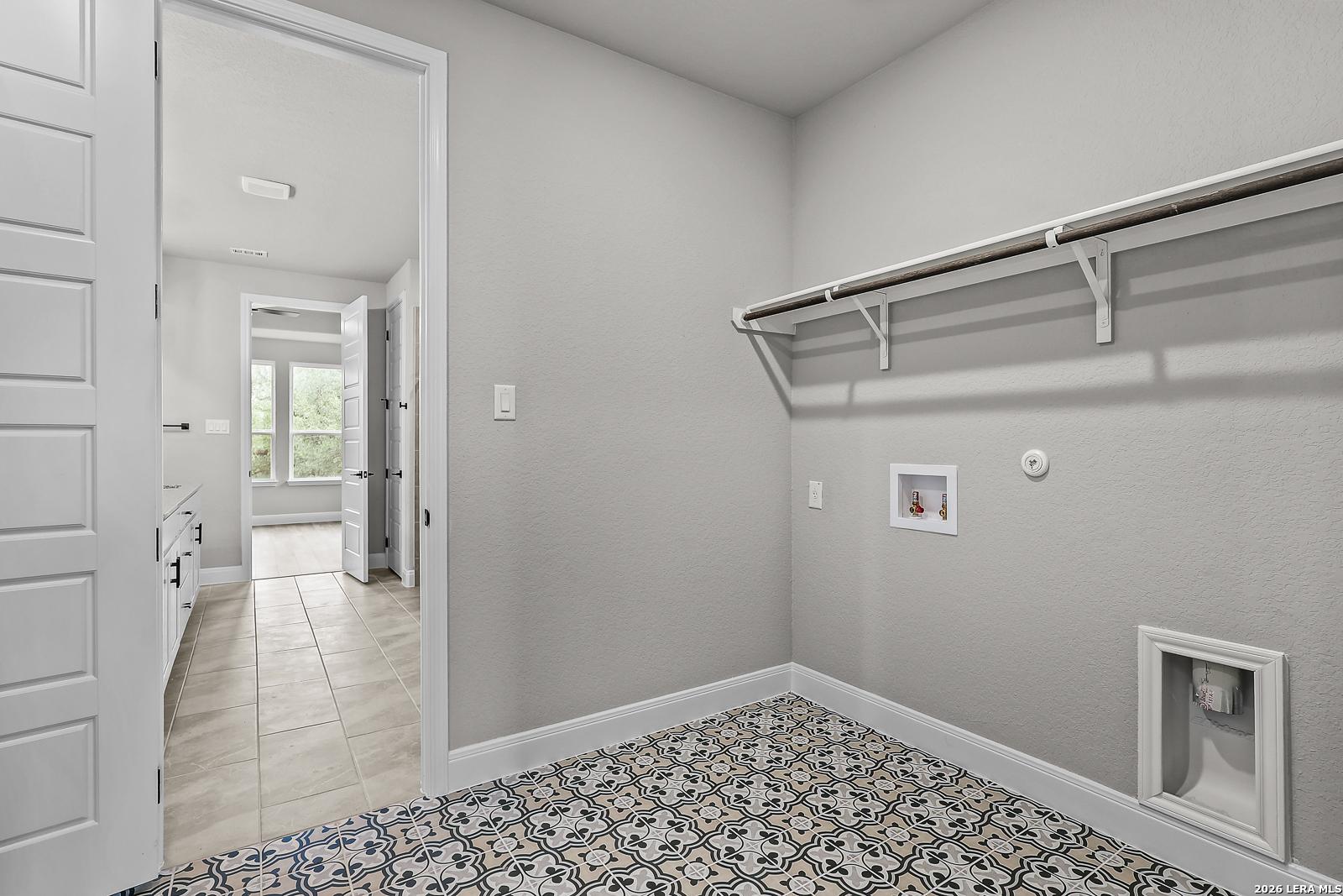 Modern laundry room featuring utility sink, washer/dryer hookups, hanging rod, and blue patterned tile floor in Davidson Homes The Belmont H, Castroville TX