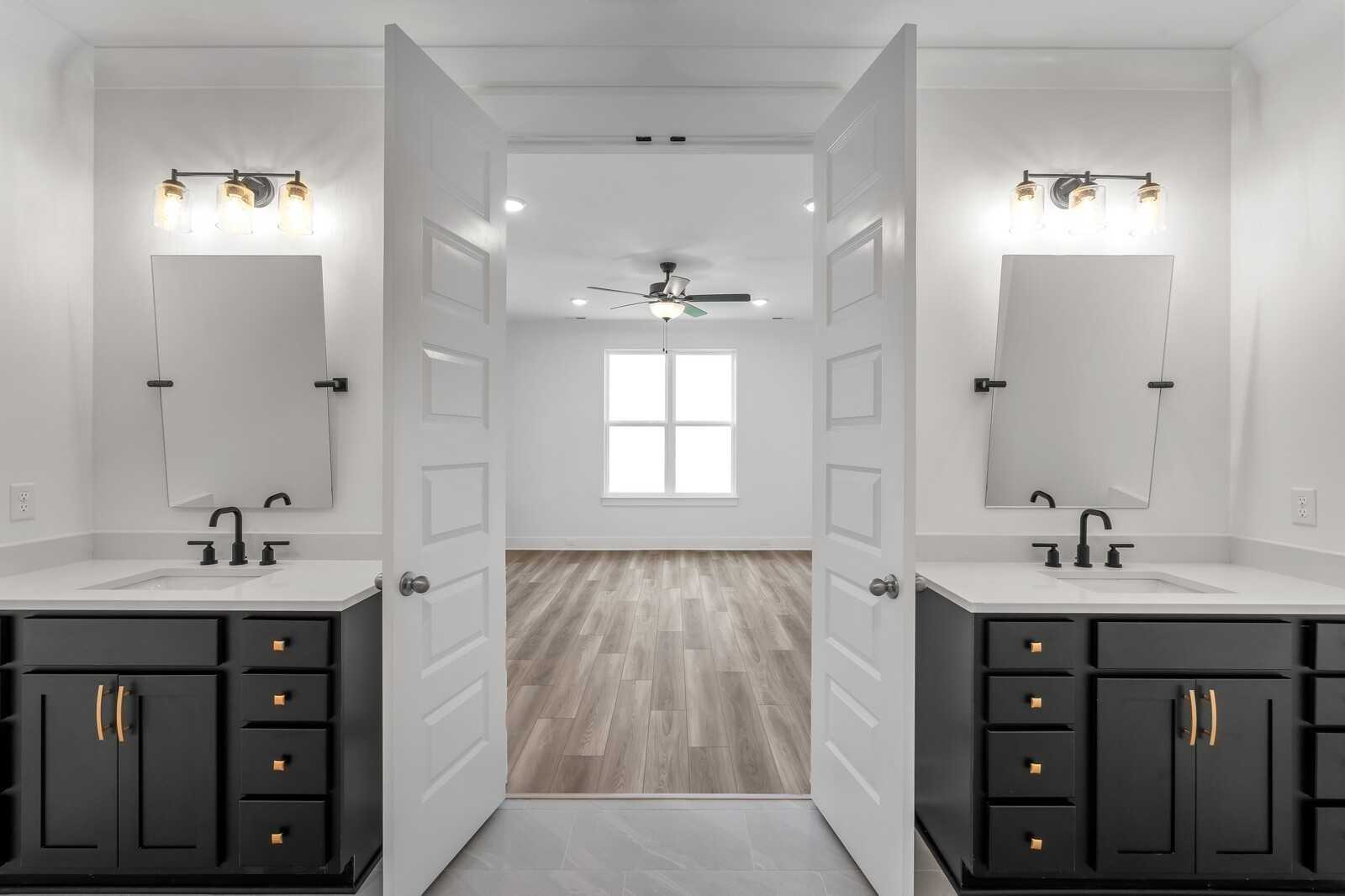 Modern master bath with dual vanities, black cabinets, mirrors, and hardwood floors opening to bedroom in Davidson Homes The Hathaway, Murfreesboro
