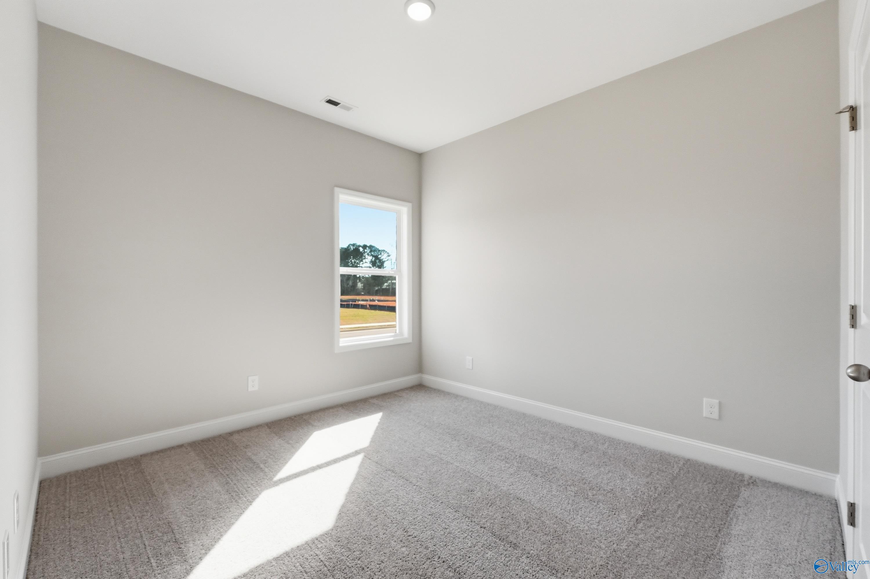 Sunlit secondary bedroom with light gray walls, beige carpet, and large window in The Asheville C, Davidson Homes, Huntsville, AL