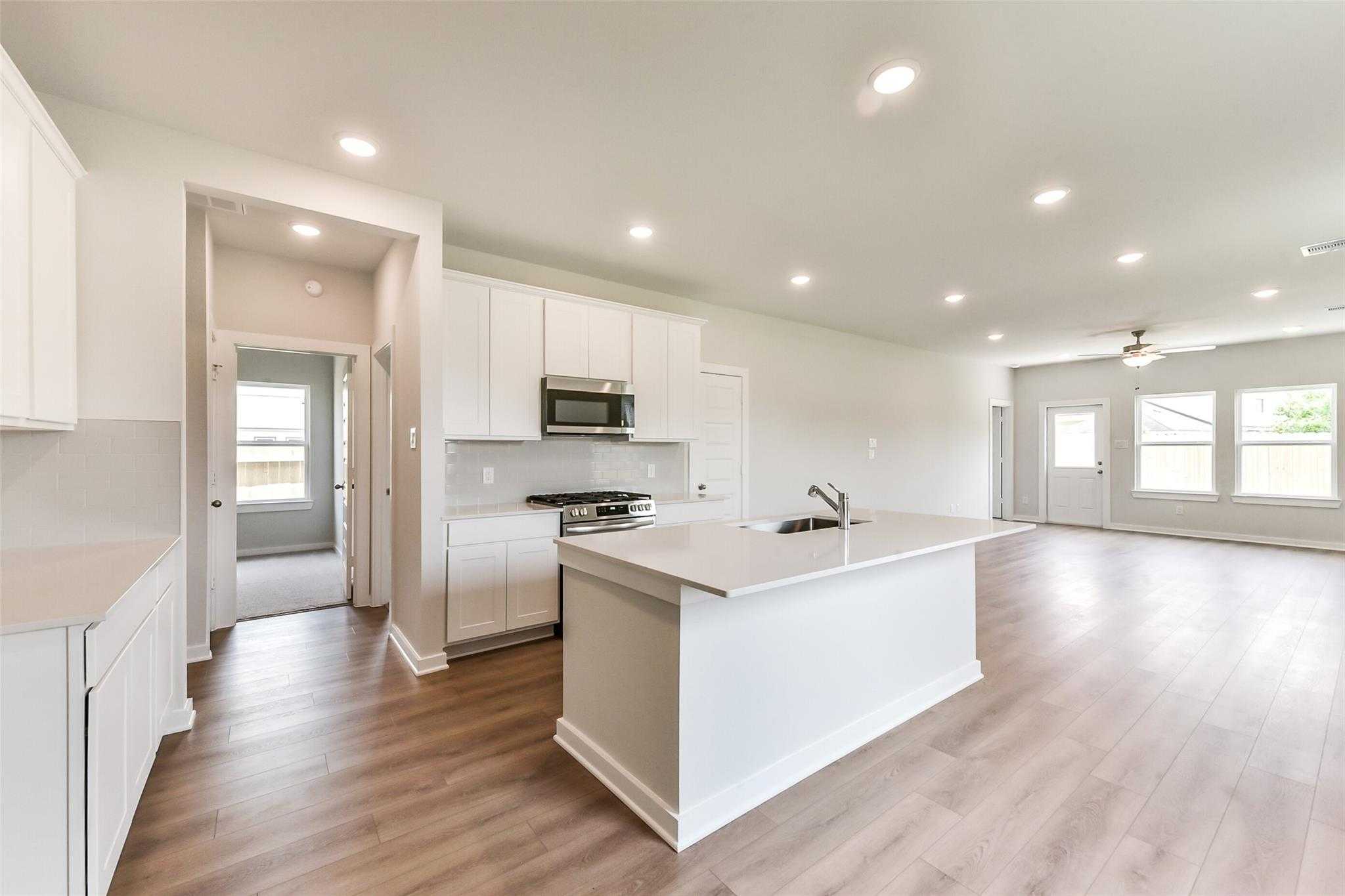 Modern open-concept kitchen with white cabinets, quartz island sink, stainless appliances in Davidson Homes The Frio F, Dayton TX