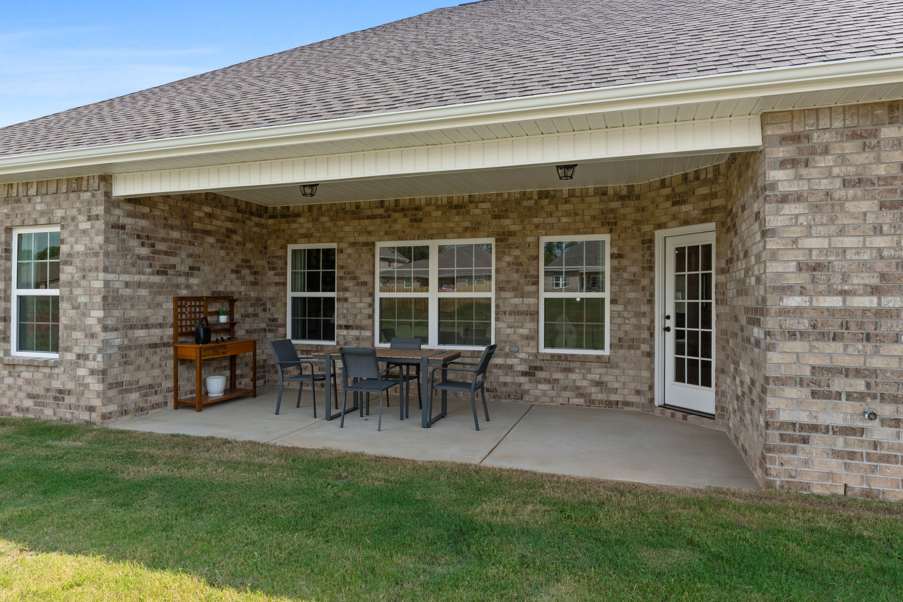 Covered patio with outdoor dining table and chairs at River Road Estates in Decatur Alabama brick home exterior lush green yard