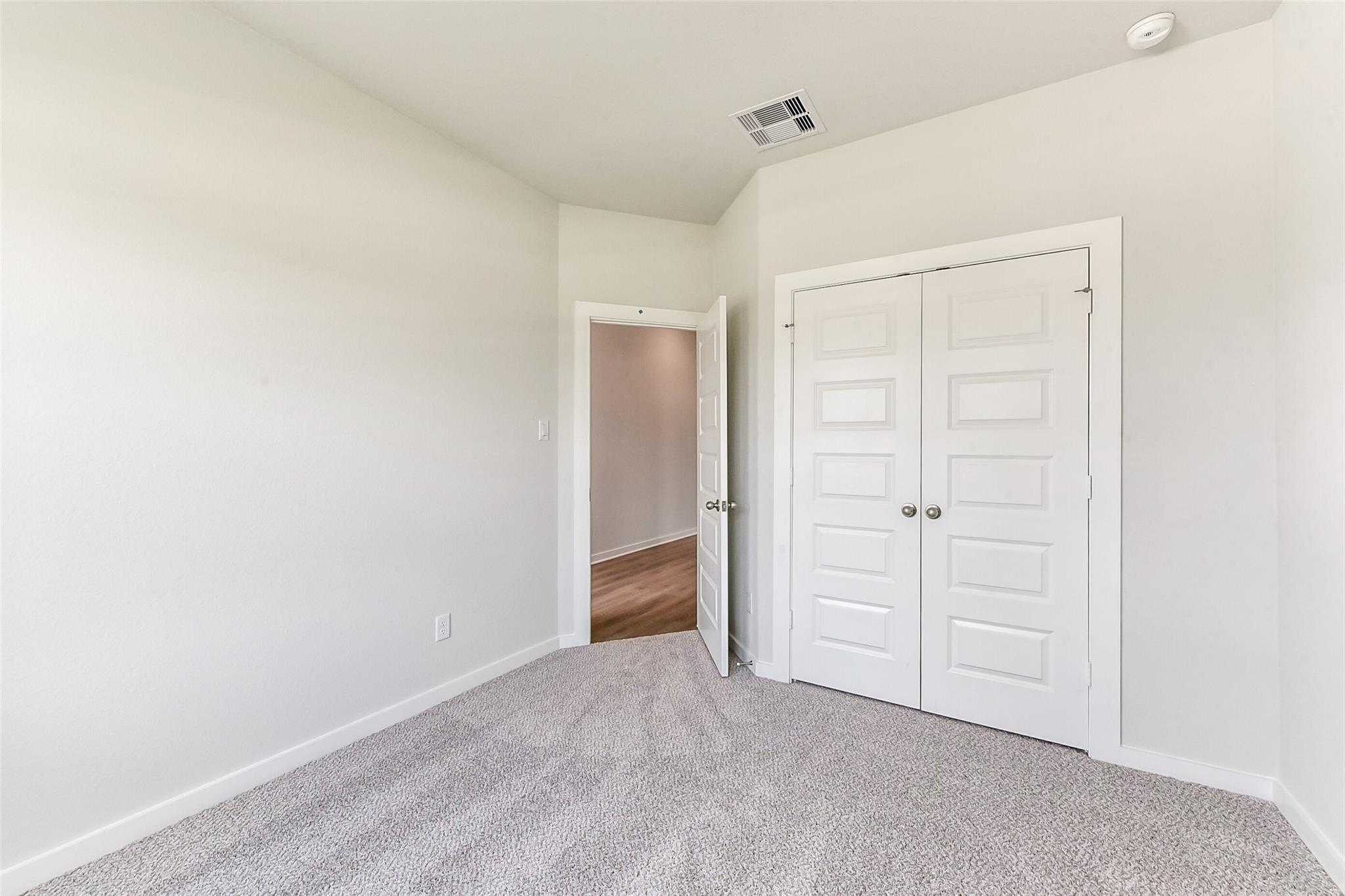 Carpeted bedroom corner with white double closet doors and open doorway in Davidson Homes The Laguna C, Rosharon, Texas