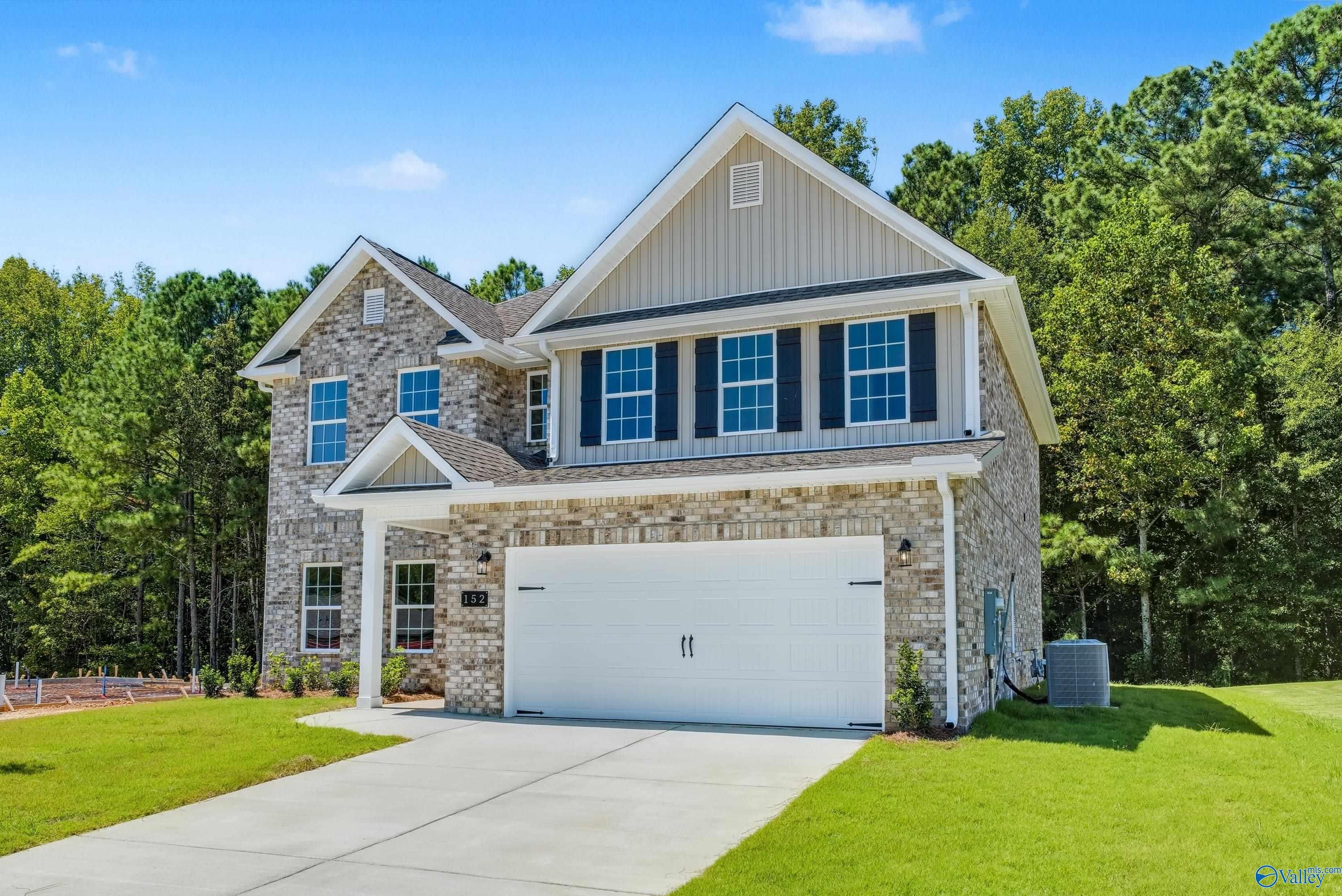 Two-story stone and siding home with 2-car garage, lush trees, and driveway in The Highlands, Arab, Alabama by Davidson Homes