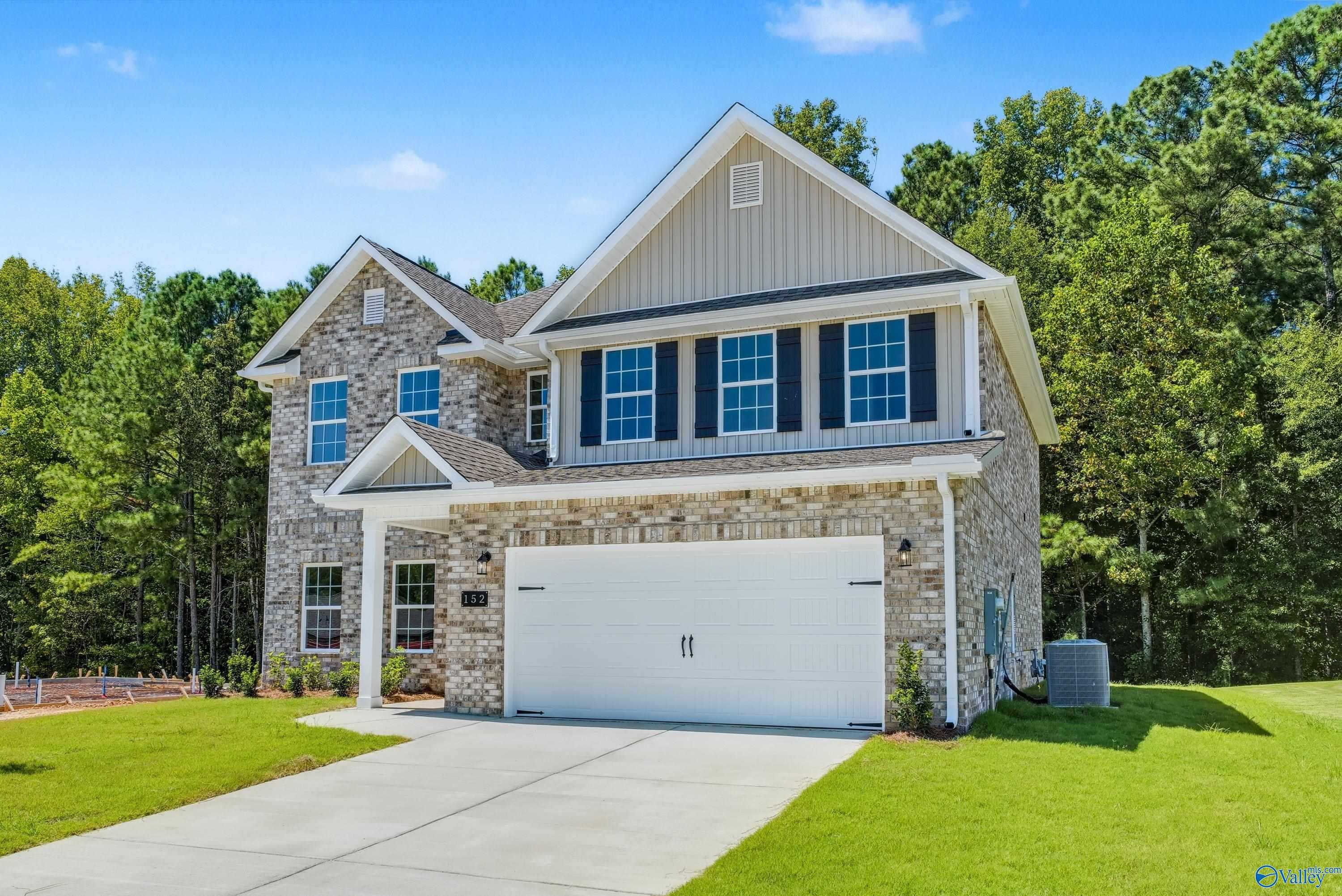 Two-story stone and siding home with 2-car garage, lush trees, and driveway in The Highlands, Arab, Alabama by Davidson Homes