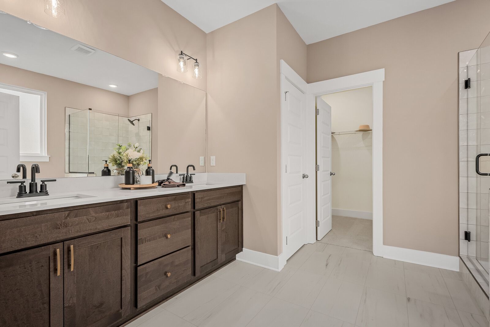 Spacious master bathroom in The Ridgeport E with double dark wood vanity, walk-in shower, and closet access