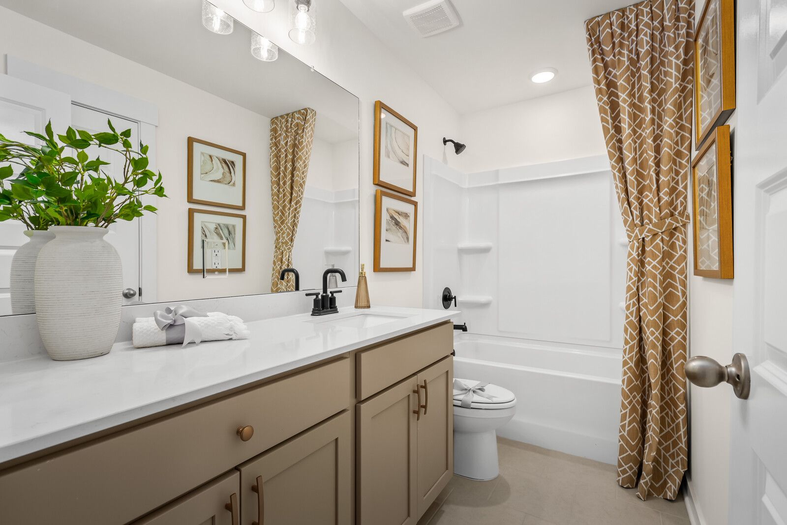 Spacious master bathroom in The Ridgeport E with quartz vanity, beige cabinets, alcove tub, patterned shower curtain, and botanical art