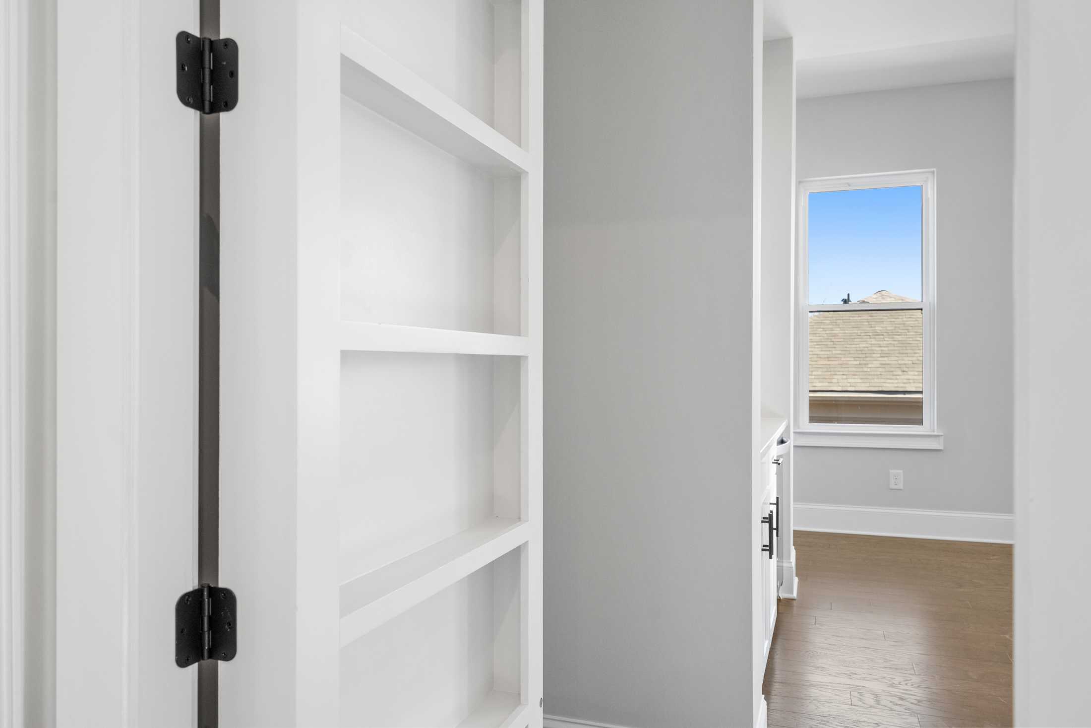 Built-in white open shelving in The Seaside A home design, gray walls, large window with sky view, hardwood floors
