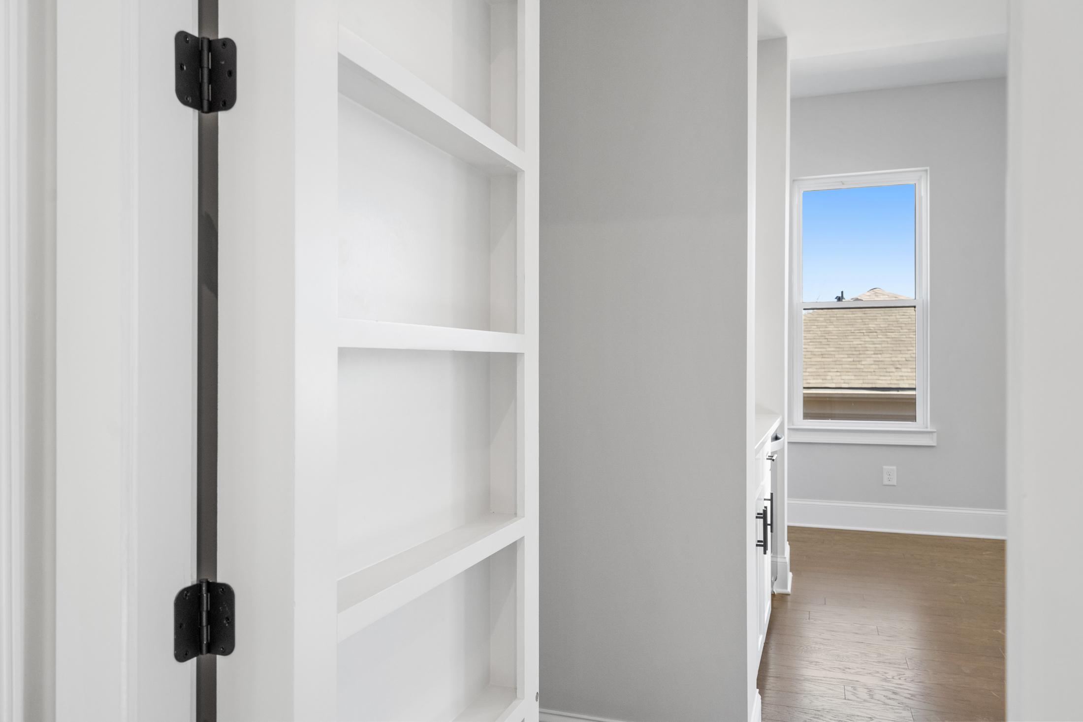Built-in white open shelving in The Seaside A home design, gray walls, large window with sky view, hardwood floors