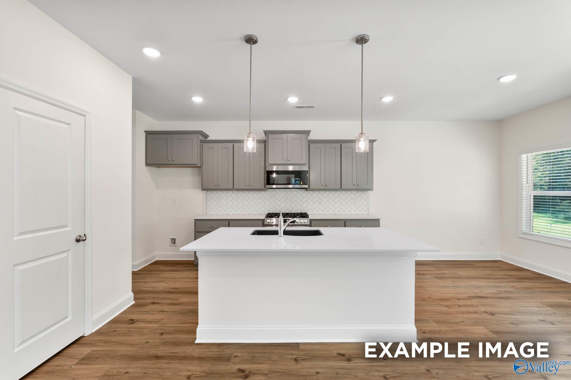 Modern kitchen featuring gray shaker cabinets, white quartz island, subway tile backsplash, and stainless appliances in Davidson Homes The Shelby A, Hazel Green, AL