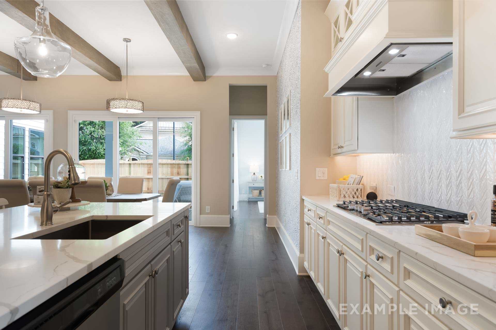 Spacious The Seaside kitchen with white cabinets, gray island sink, gas range, herringbone backsplash, and open view to patio