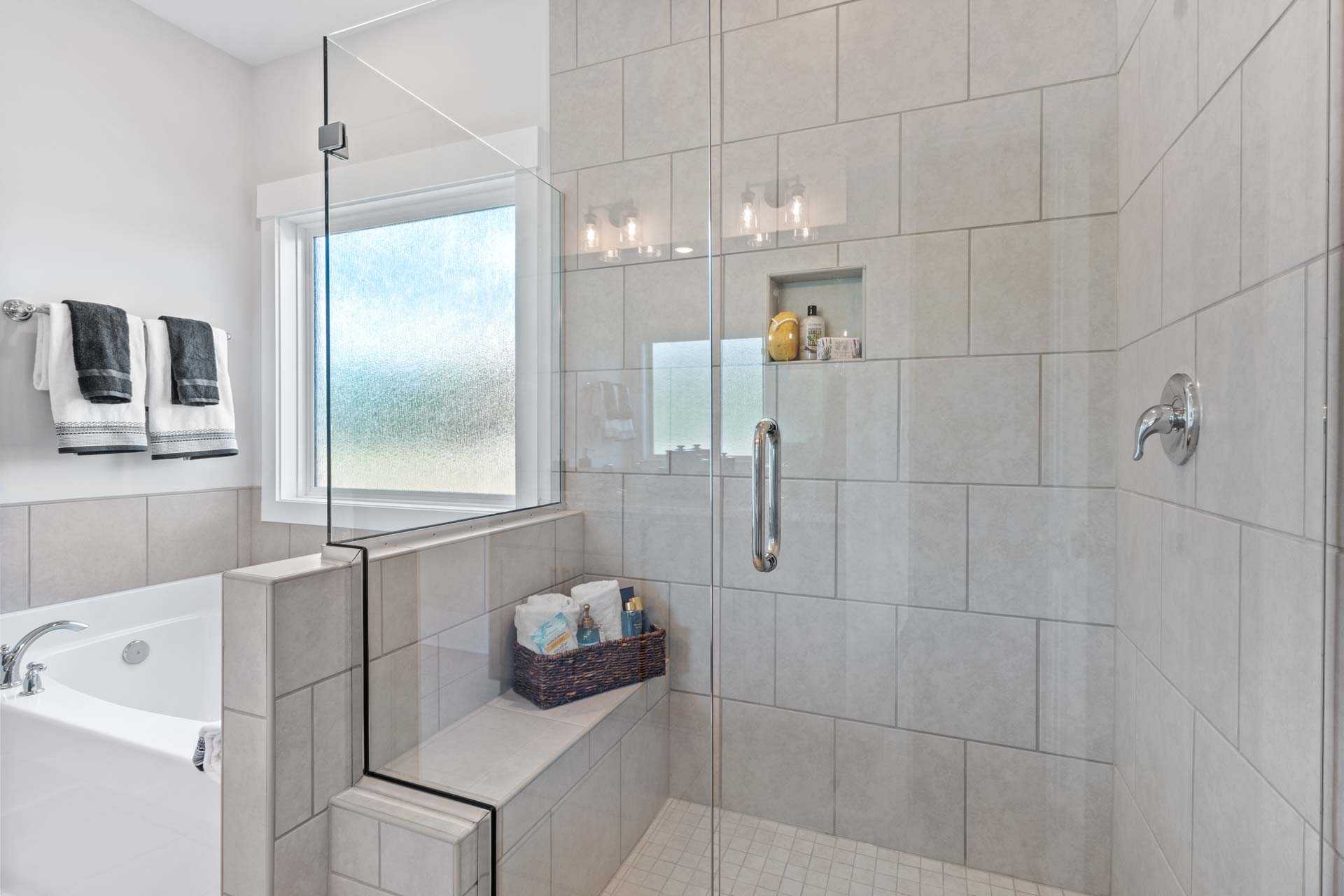 Spacious master bathroom in Blue Spring Huntsville AL with walk-in glass shower, freestanding tub, tiled walls, frosted window