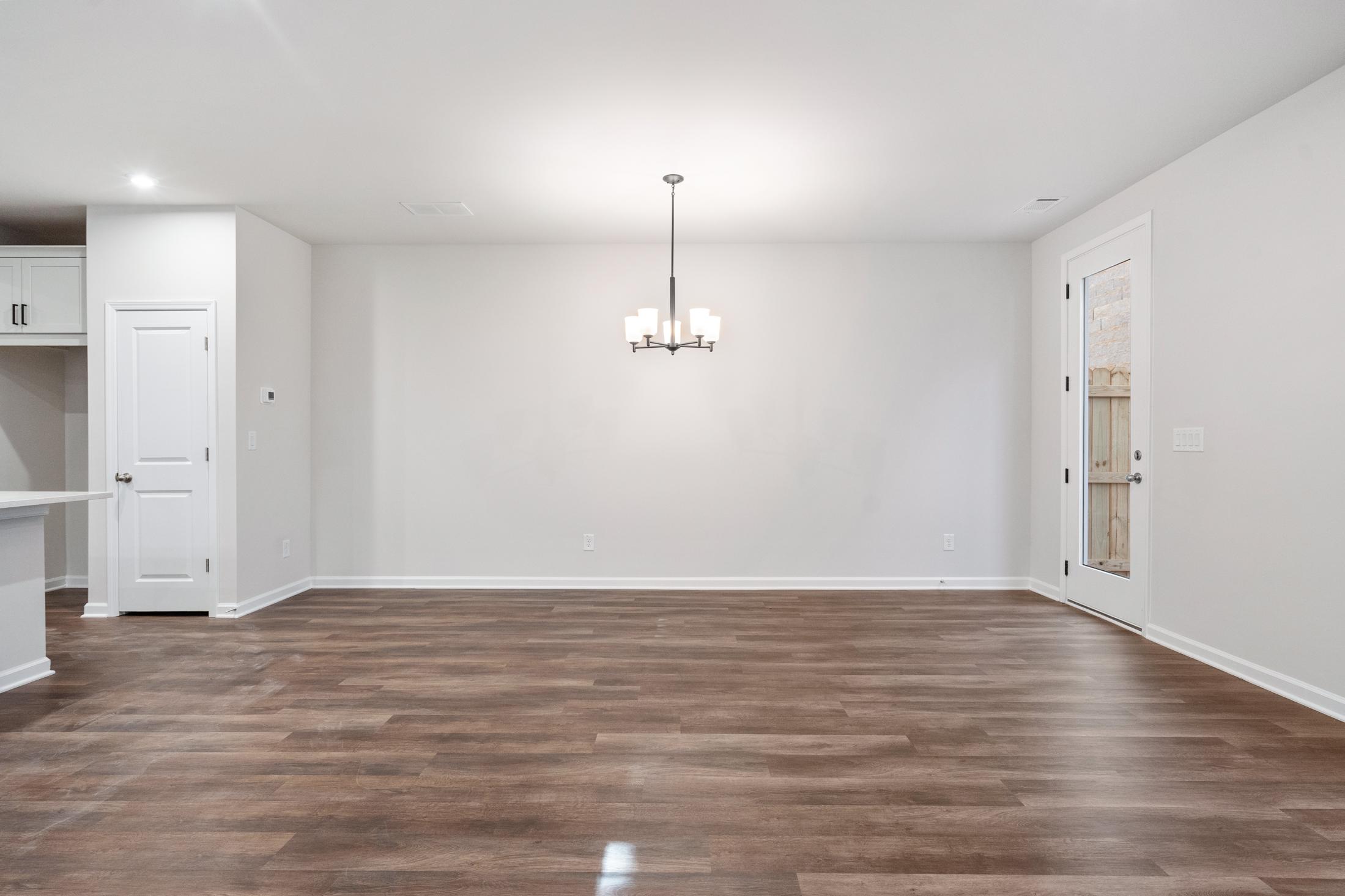 Spacious open-concept dining area in The Cary B home featuring hardwood floors, white cabinetry, and chandelier lighting