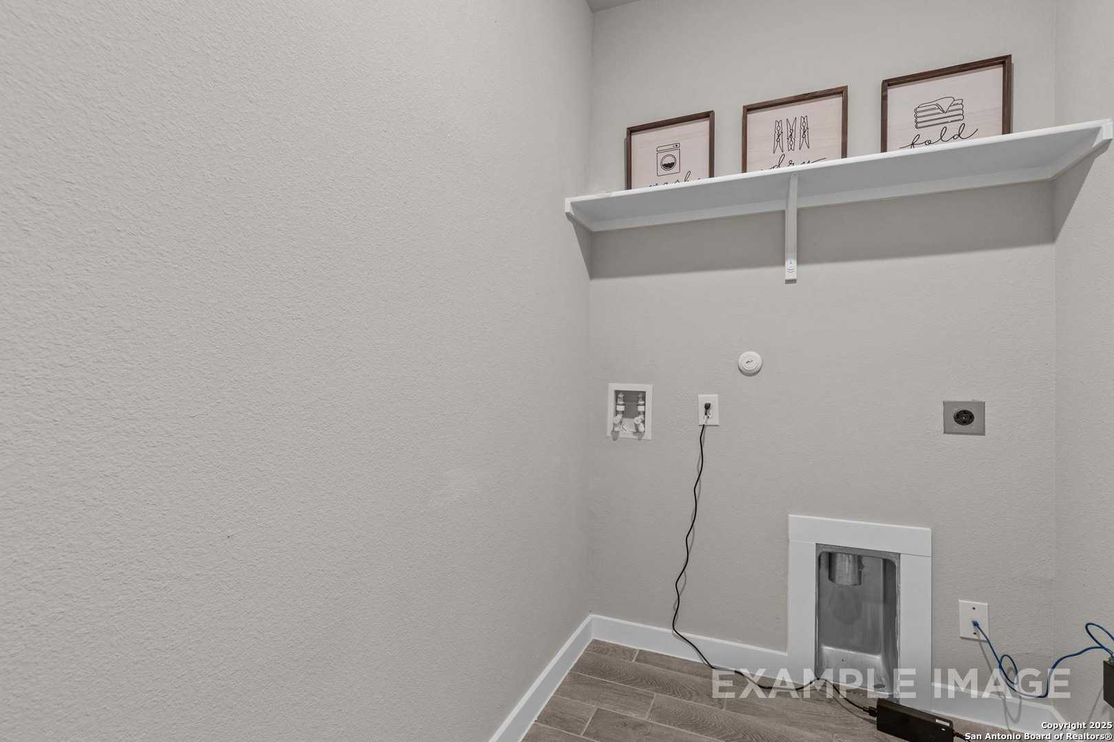 Modern laundry room with washer-dryer hookups, floating shelf, and framed art in Davidson Homes The Collin B, Seguin, Texas