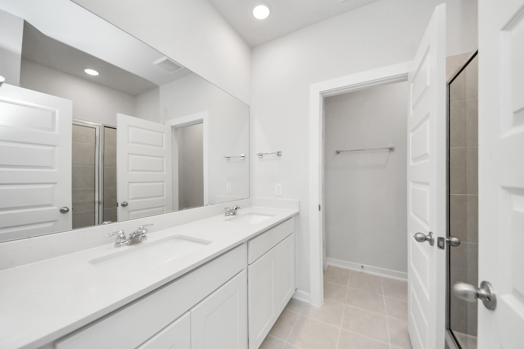 Modern primary bathroom with double vanity and walk-in closet in The Frio F floor plan at Liberty Estates, Cleveland, Texas.