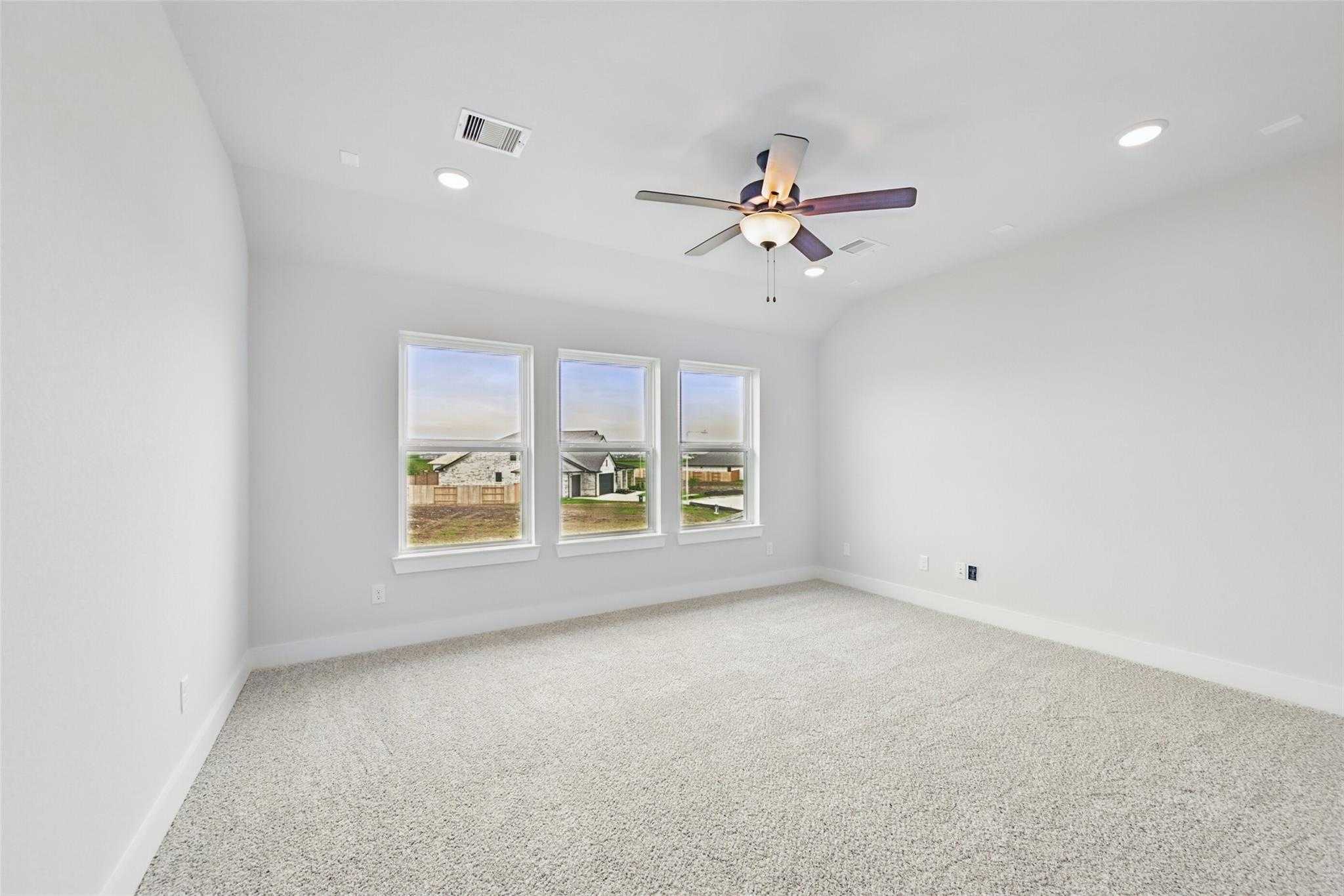 Bright empty bedroom with ceiling fan, recessed lights, and triple windows overlooking fields in Davidson Homes The Victoria C, Lago Mar, Texas City