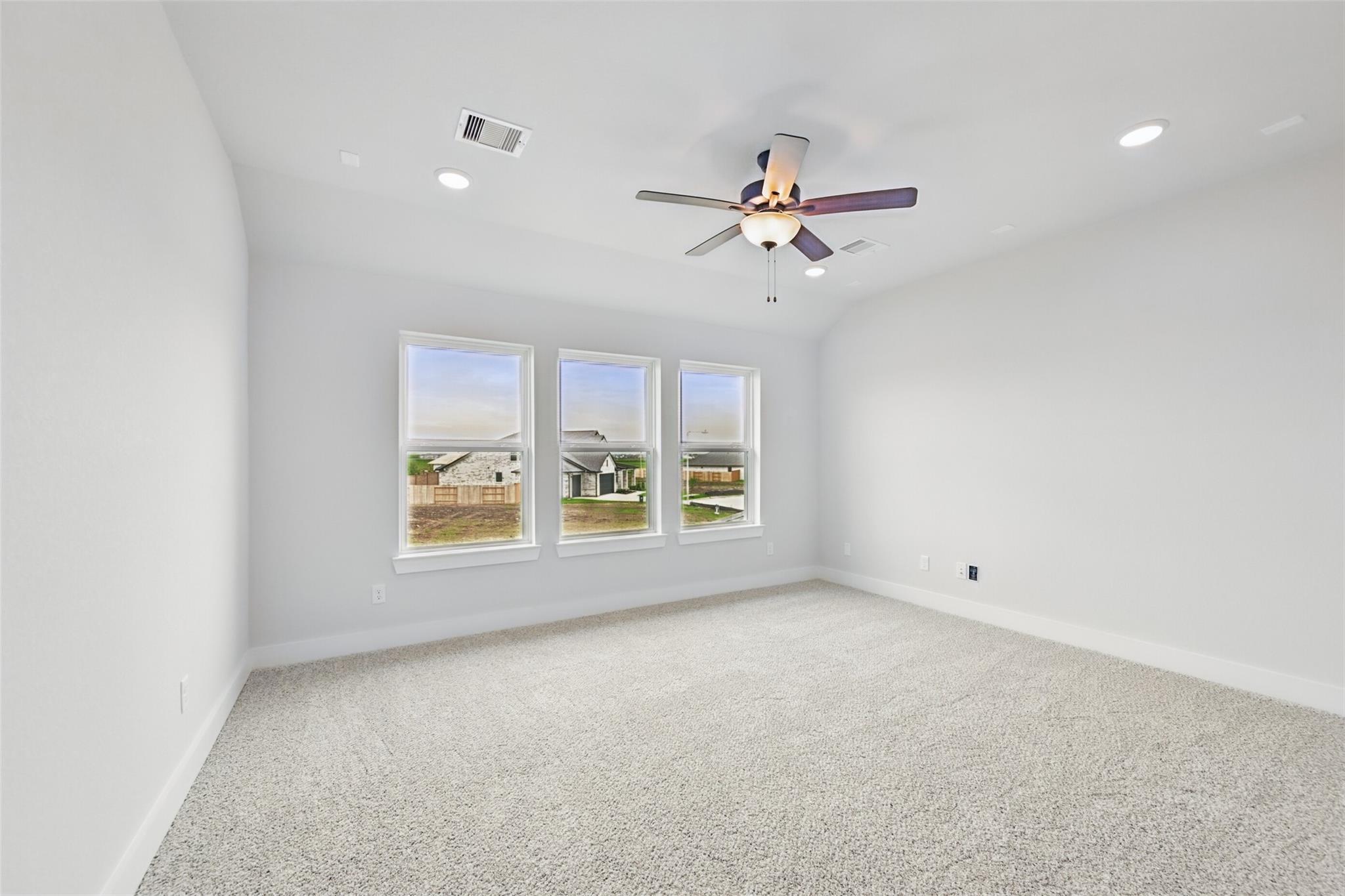 Bright empty bedroom with three large windows, ceiling fan, white walls, and carpet in Davidson Homes The Victoria C, Lago Mar, Texas City
