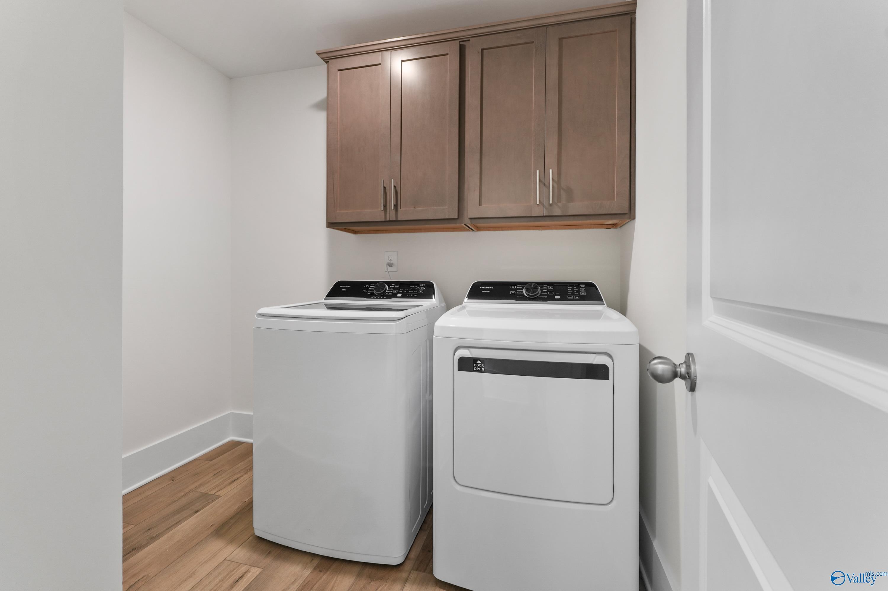Modern laundry room with white front-load washer, dryer, and shaker cabinets in Davidson Homes The Daphne C, Arab, Alabama