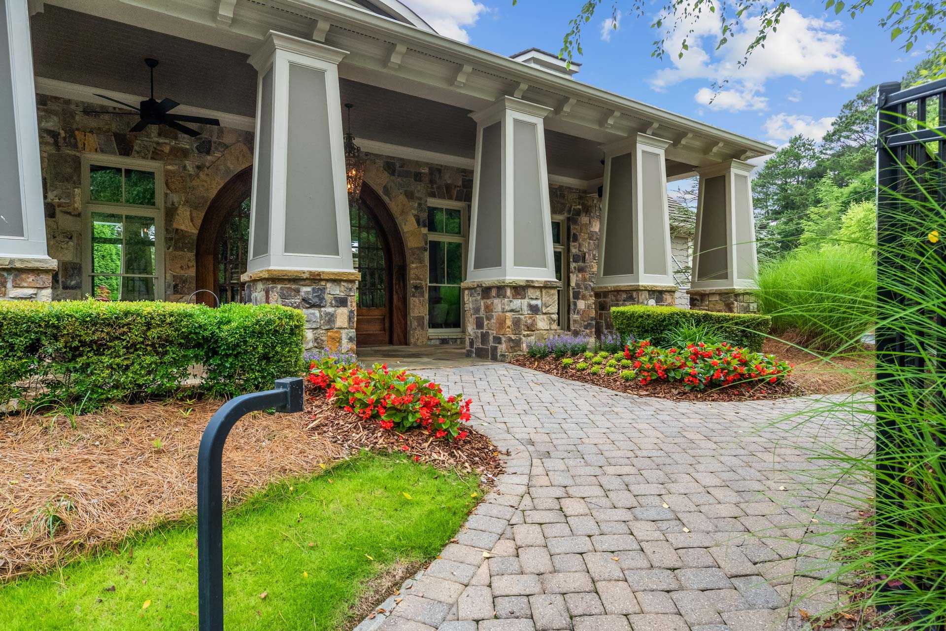 Stone-front home exterior at The Village at Towne Lake in Woodstock Georgia with covered porch columns arched entry and red flower beds