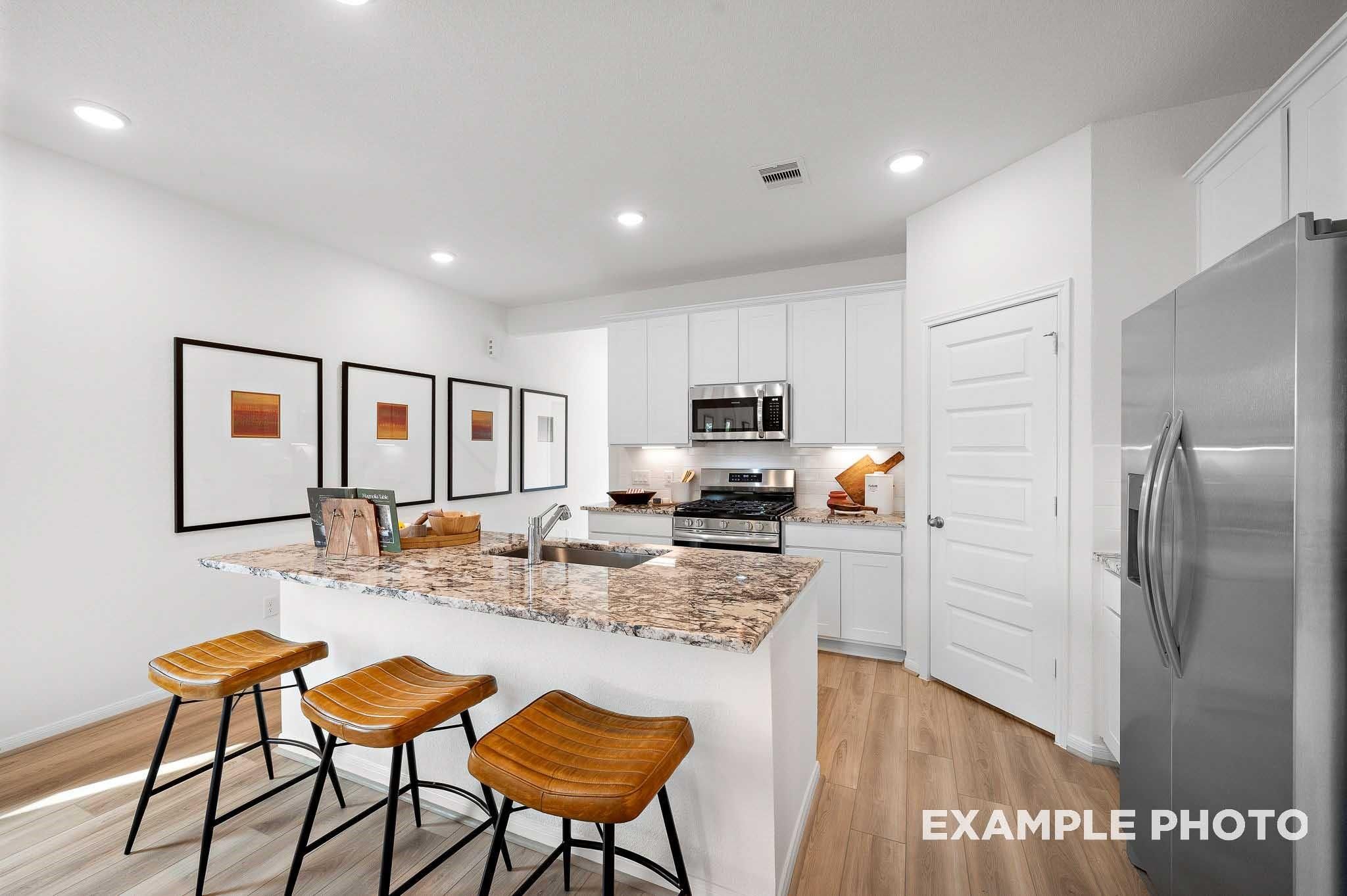 Modern kitchen featuring white shaker cabinets, granite island with bar stools, stainless appliances in Davidson Homes The Sabine F, Magnolia, Texas
