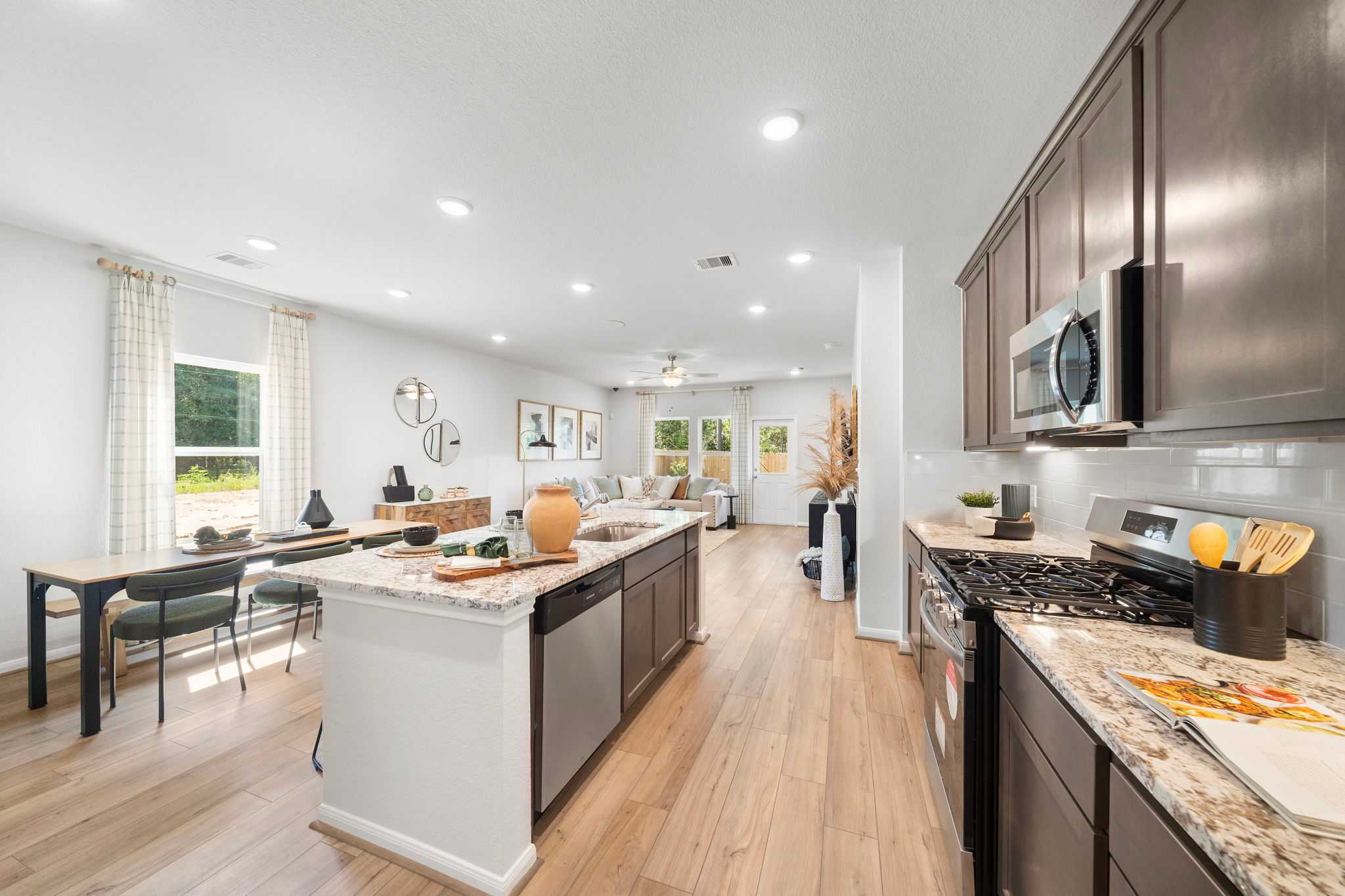 Open-concept kitchen at Caney Creek Place in Conroe Texas with hardwood floors dark cabinets white island and dining area