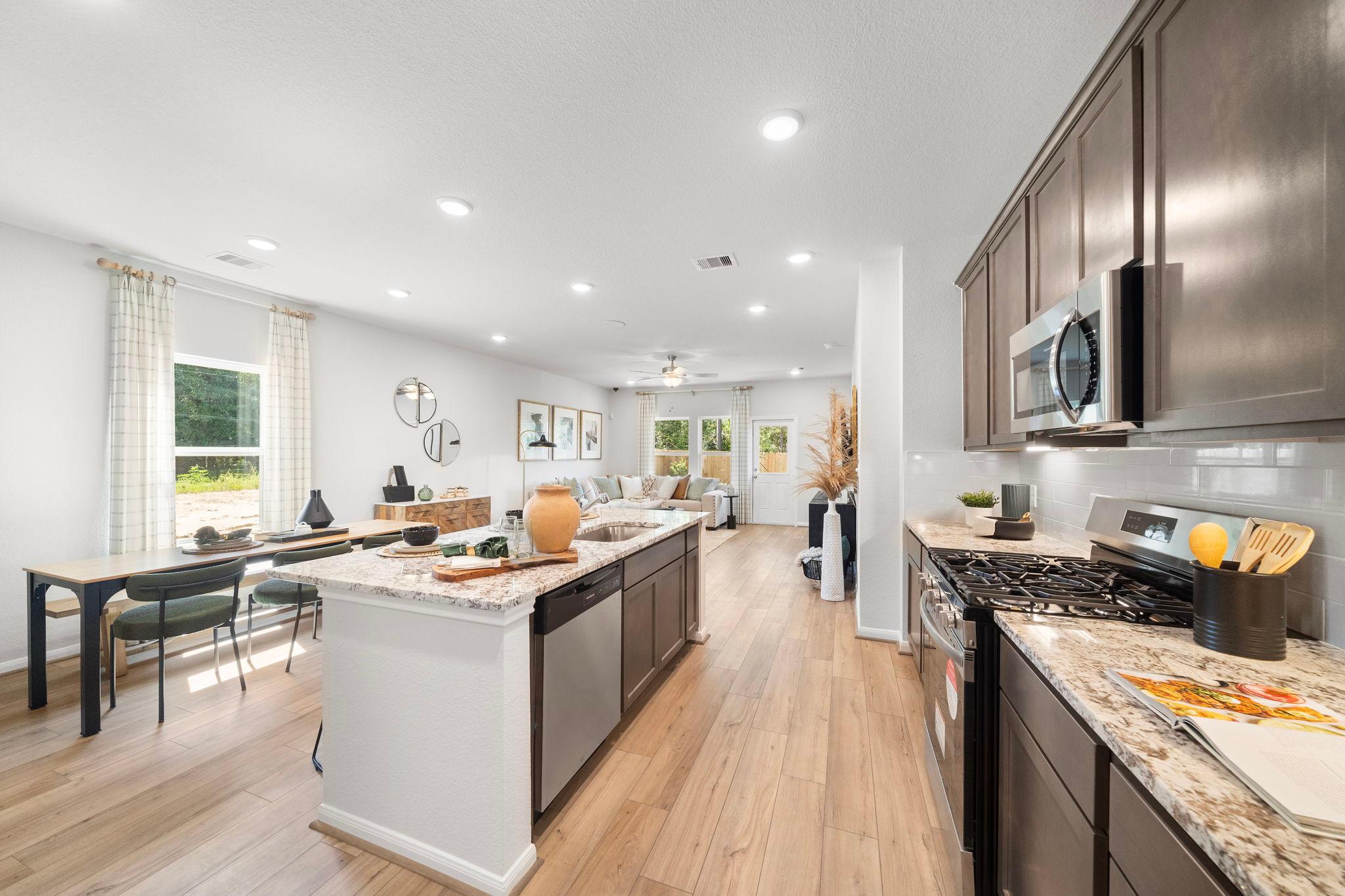 Open-concept kitchen at Caney Creek Place in Conroe Texas with hardwood floors dark cabinets white island and dining area