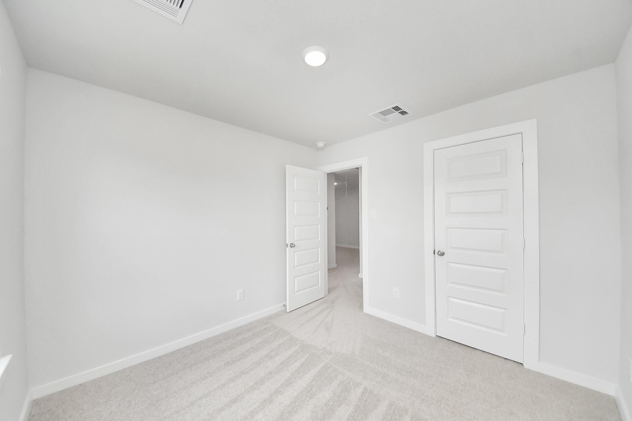 Bright bedroom with plush carpet and white doors in The Blanco E floor plan by Davidson Homes in Conroe, Texas.