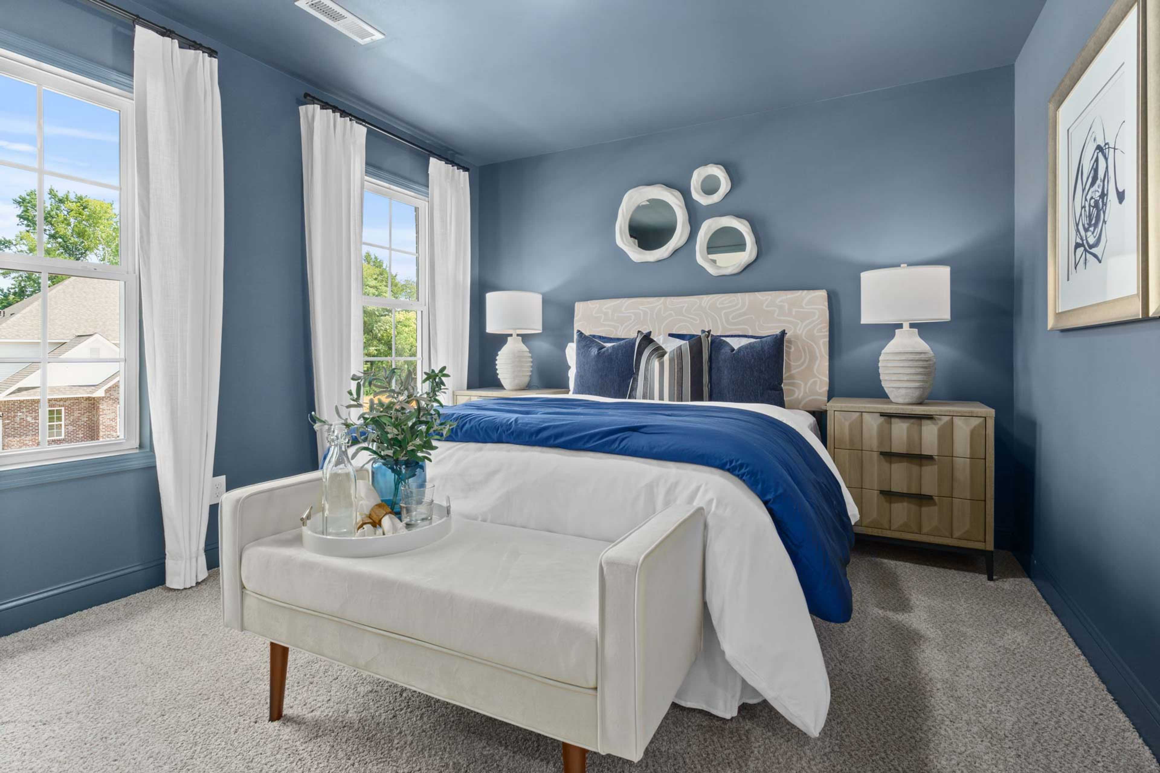 Spacious primary bedroom at Creek Grove in New Market Alabama with navy blue walls, king bed, white bench, and large windows