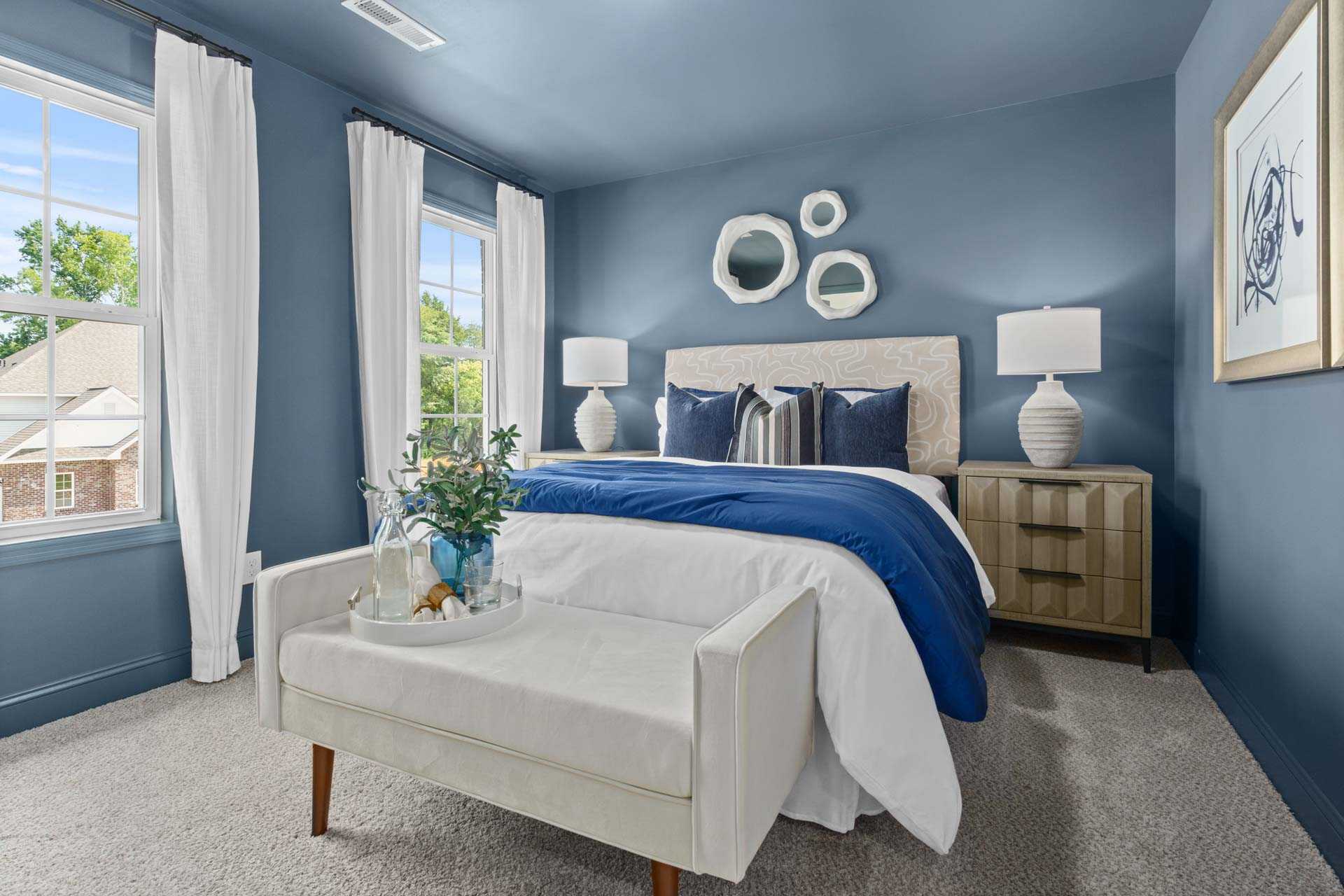 Spacious primary bedroom at Creek Grove in New Market Alabama with navy blue walls, king bed, white bench, and large windows