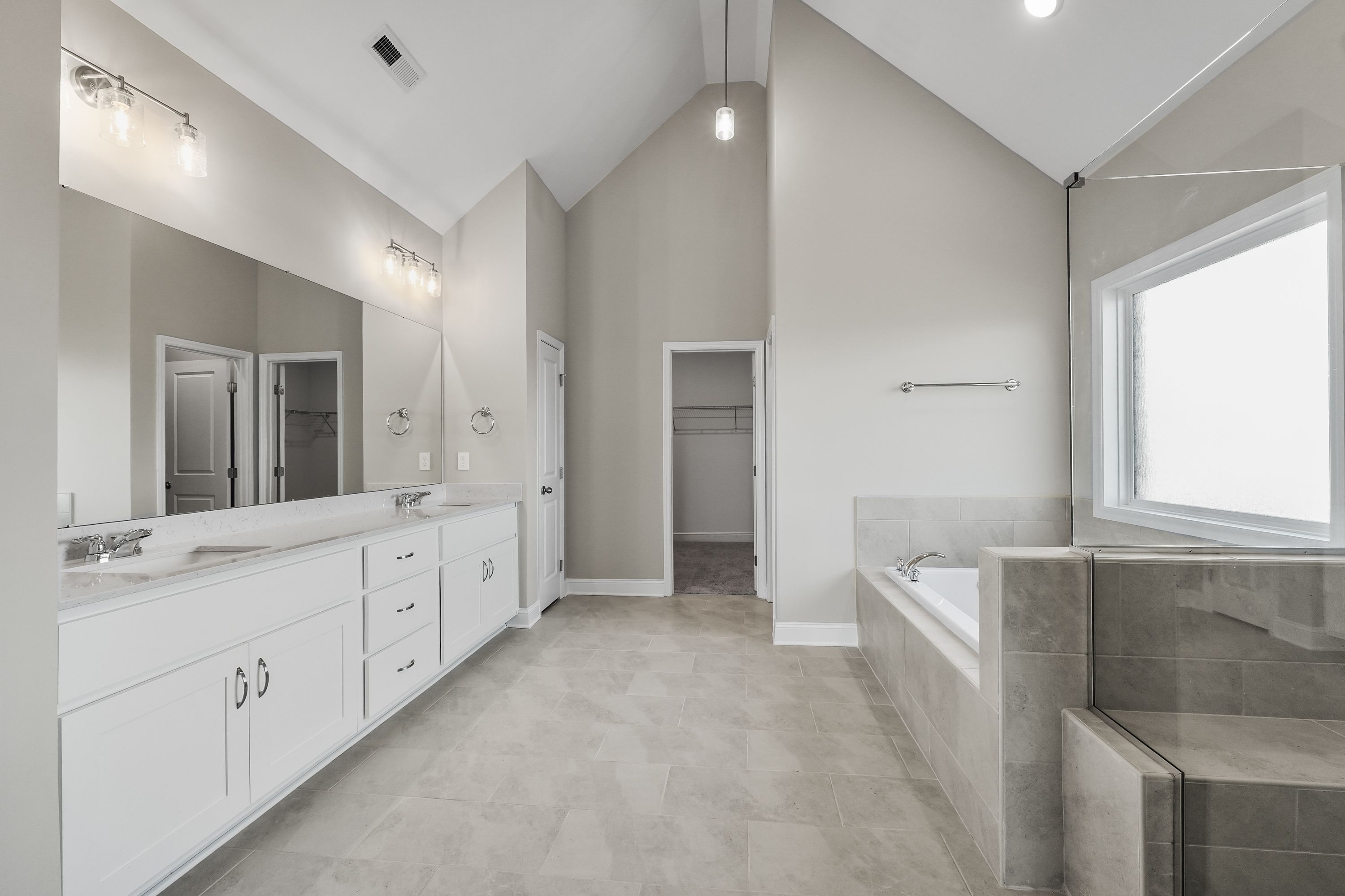 Spacious master bathroom in The Valencia with dual vanities, freestanding tub, walk-in shower, and vaulted ceiling