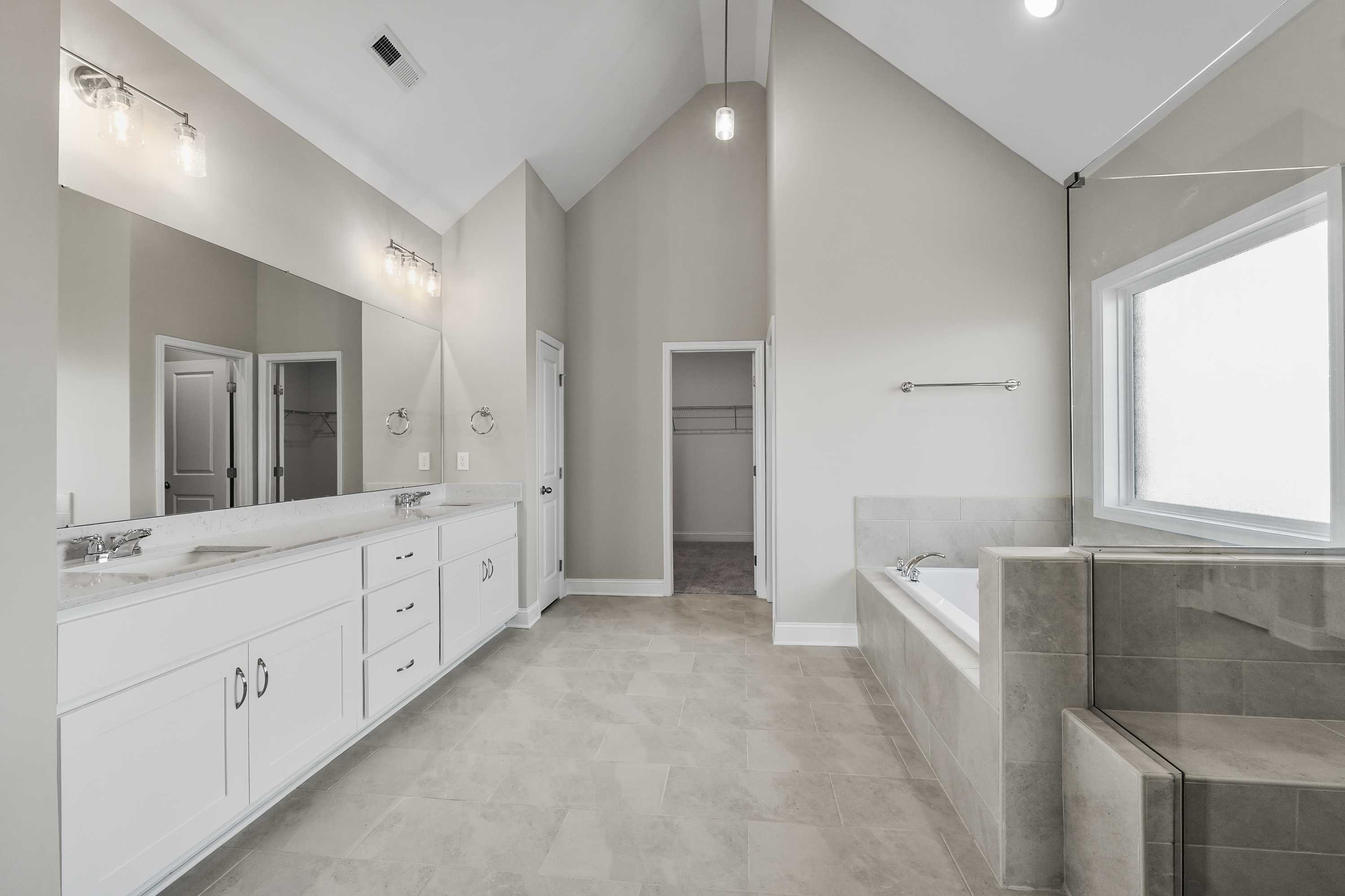 Spacious master bathroom in The Valencia with dual vanities, freestanding tub, walk-in shower, and vaulted ceiling