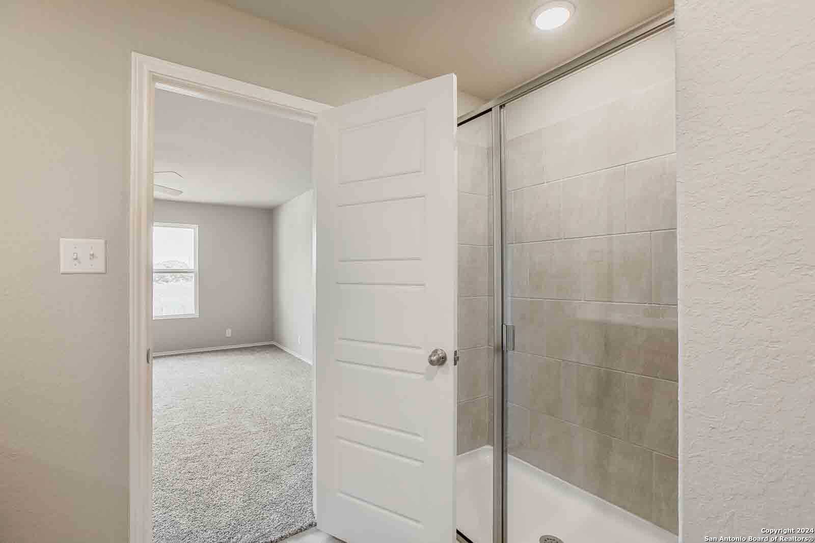 Modern en-suite bathroom with frameless glass shower and beige tile walls in Davidson Homes The Murray H, Seguin, Texas