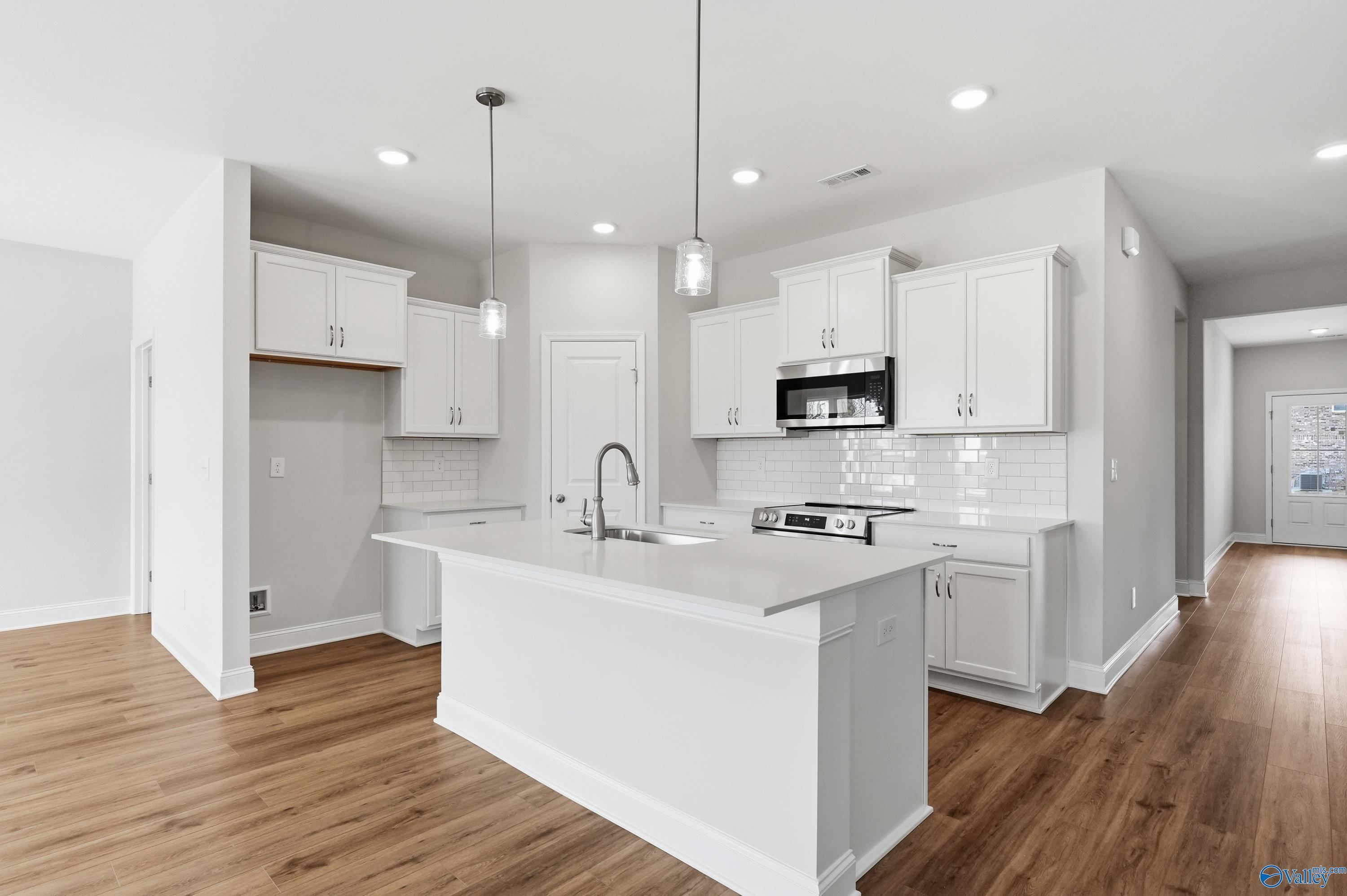 Modern white kitchen with large island sink, stainless steel appliances, subway tile backsplash in Davidson Homes The Daphne C, Toney, AL