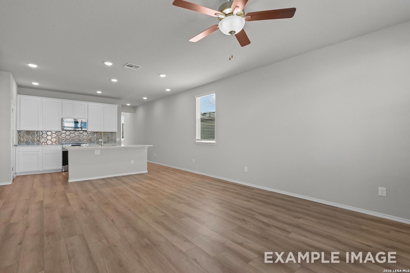 Open-concept kitchen-living area with white shaker cabinets, subway tile backsplash, island, and hardwood floors in Davidson Homes The Colorado D, Agave, San Antonio