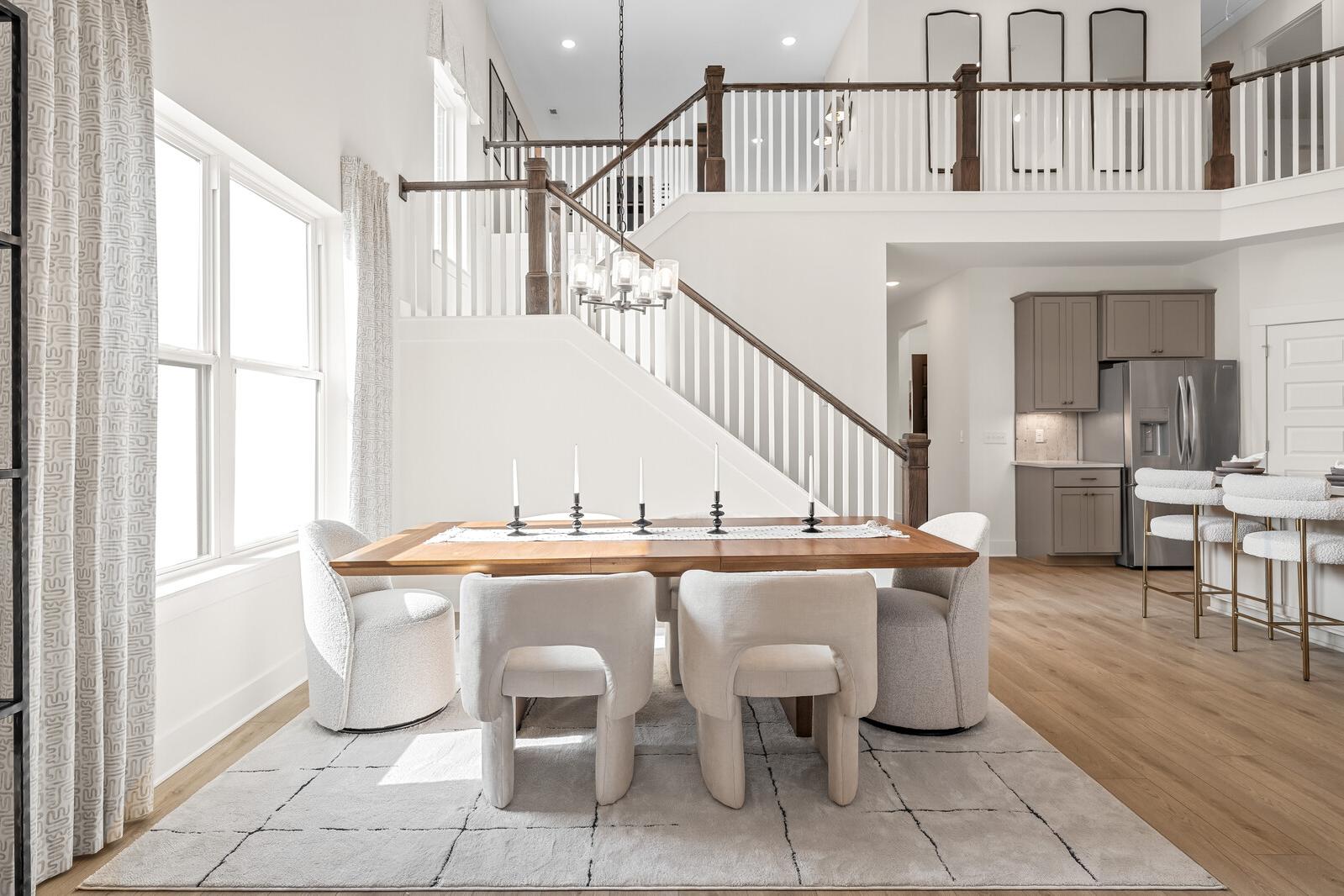 Spacious open dining area with wooden table, white chairs, and candles in Benders Cove home, Mt. Juliet TN, featuring kitchen, staircase, and balcony by Davidson Homes