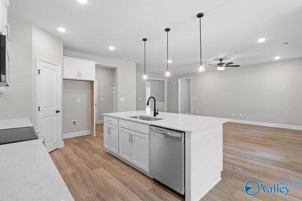 Modern white kitchen island with sink, dishwasher, and pendant lights in open-concept The Montgomery B home, Hartselle, Alabama