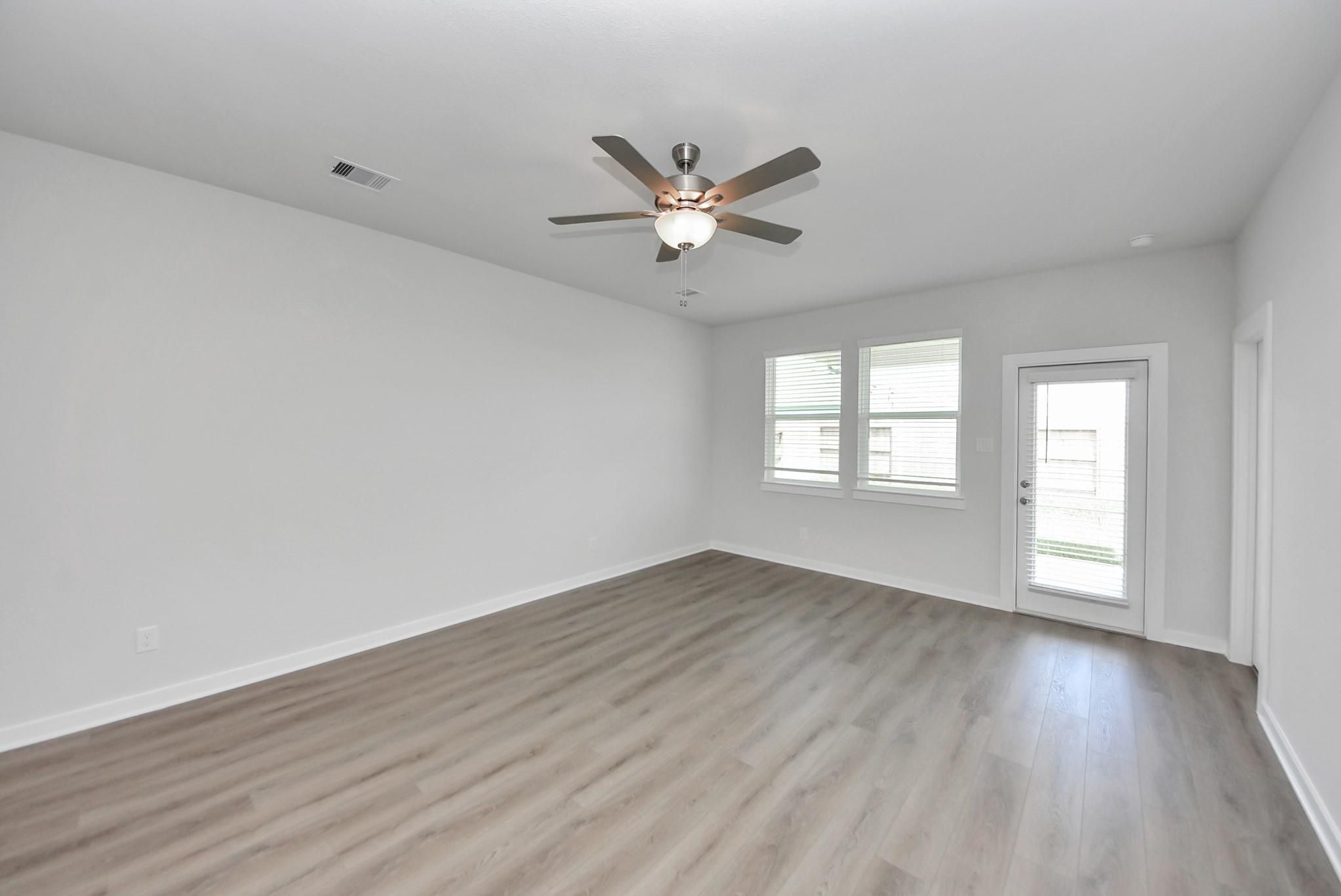 Bright empty room with luxury vinyl plank flooring, ceiling fan, and glass-paneled exterior door in Davidson Homes San Marcos E plan