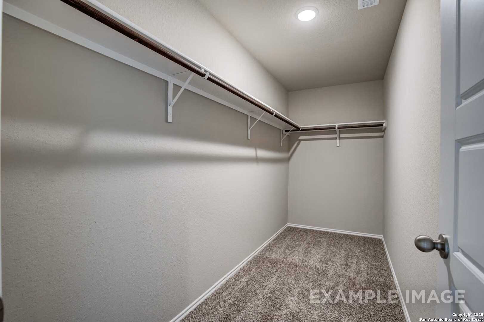 Spacious walk-in closet with built-in wooden shelves and beige carpet in Davidson Homes The Murray K, San Antonio, Texas